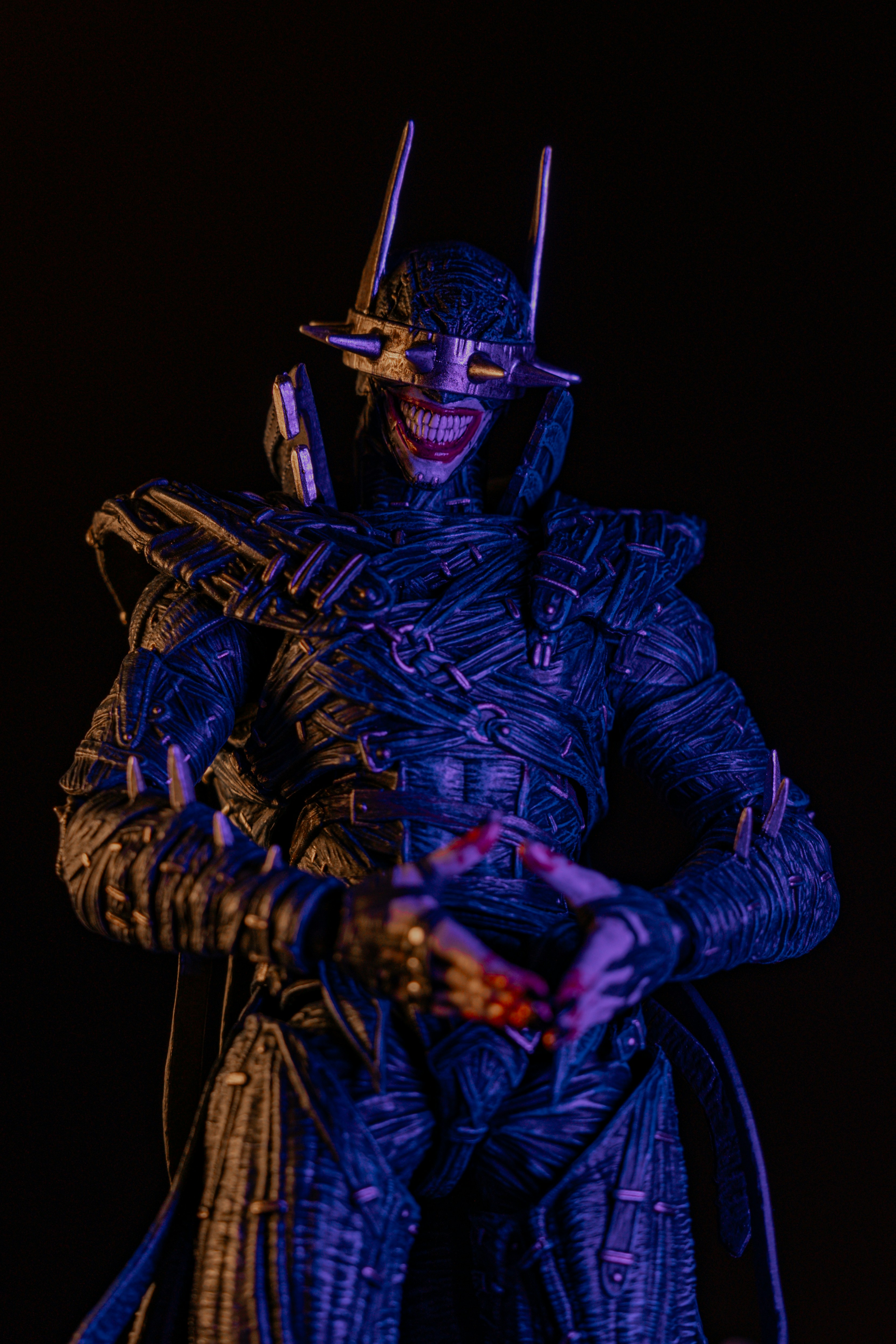 A dark action figure with a spiked visor and wide grin against black