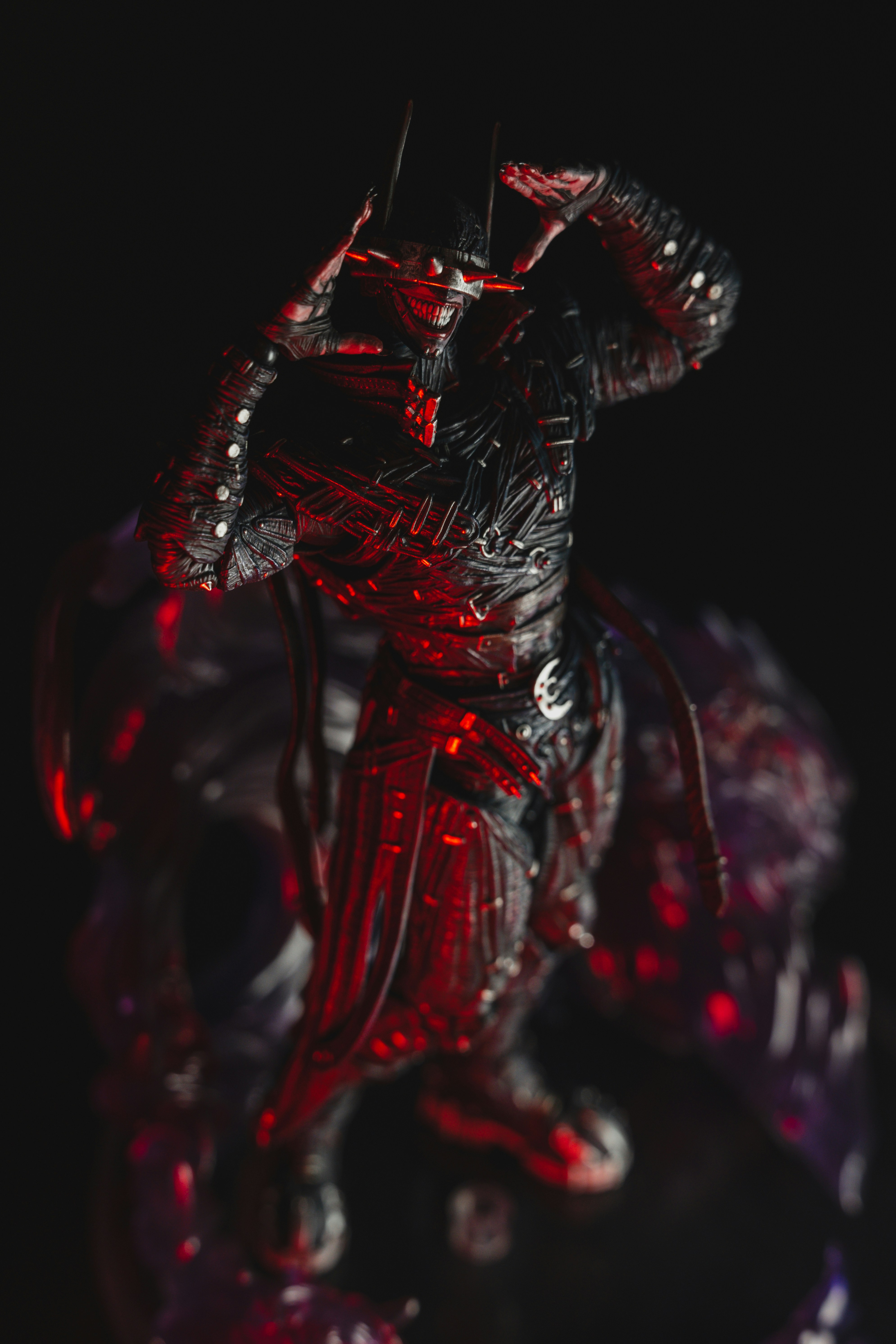 A dark action figure with a spiked visor and grin in red lighting