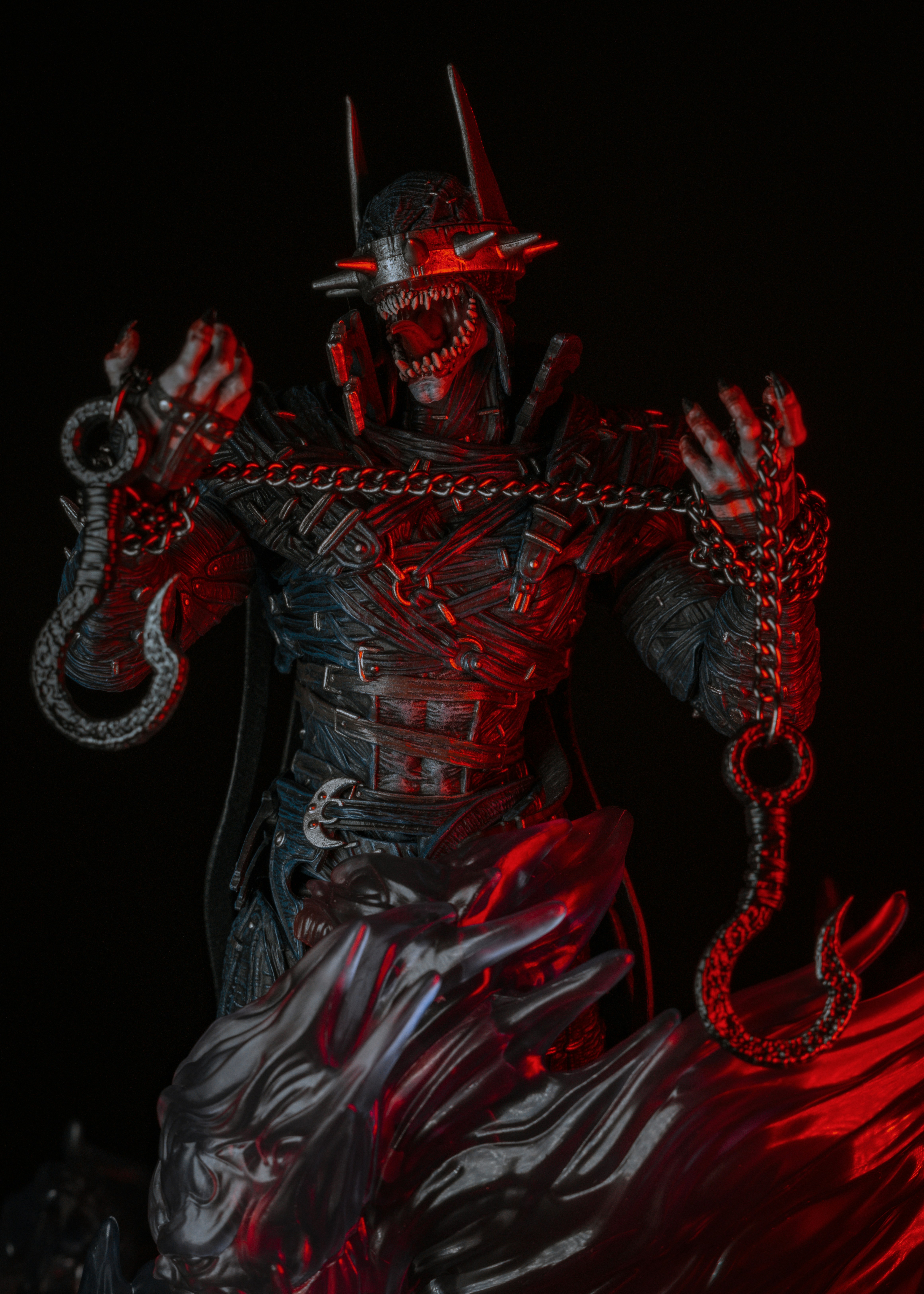 A monstrous figure in a spiked cowl holding chains with hooks under red light
