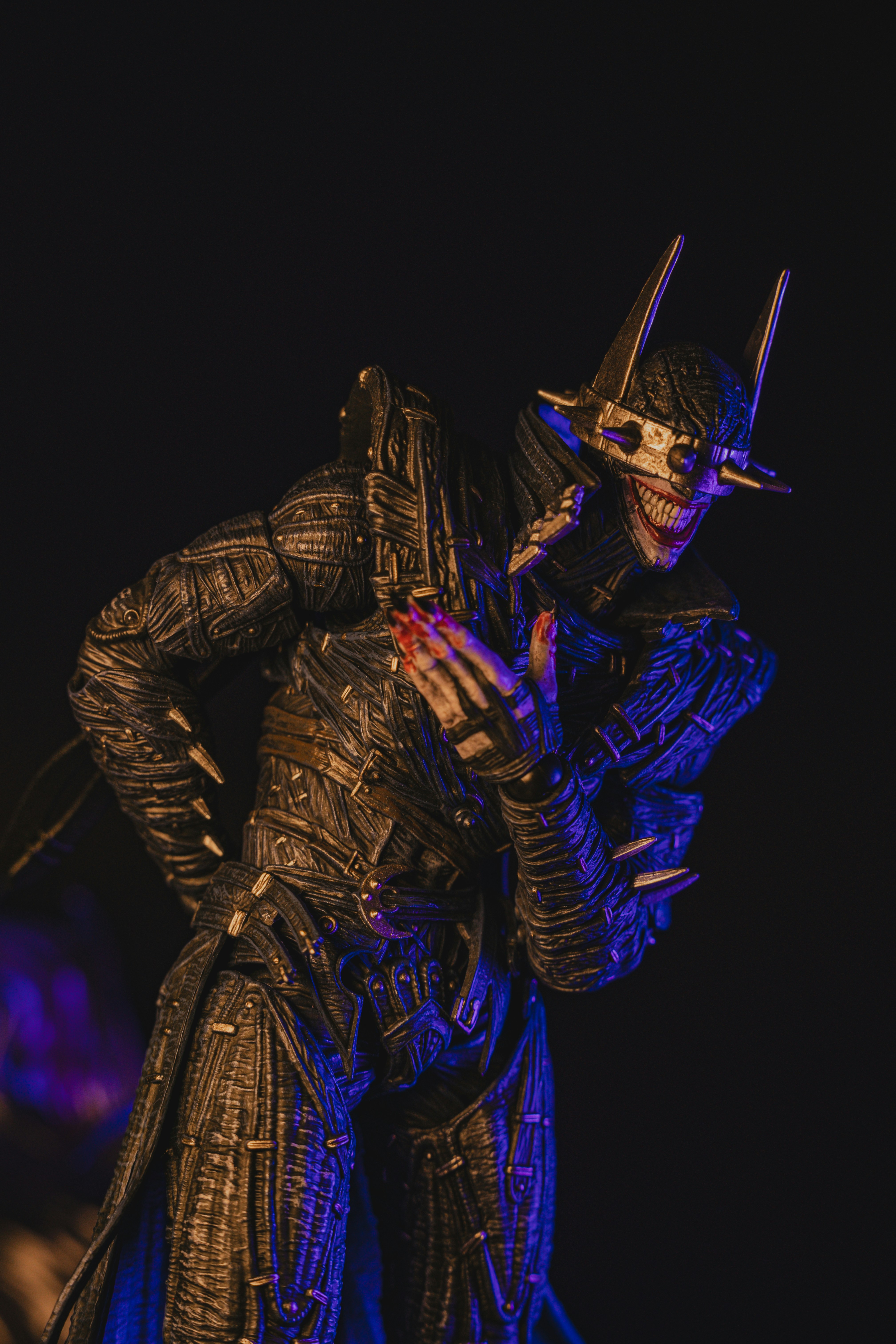 A dark action figure with a spiked crown and wide grin against black