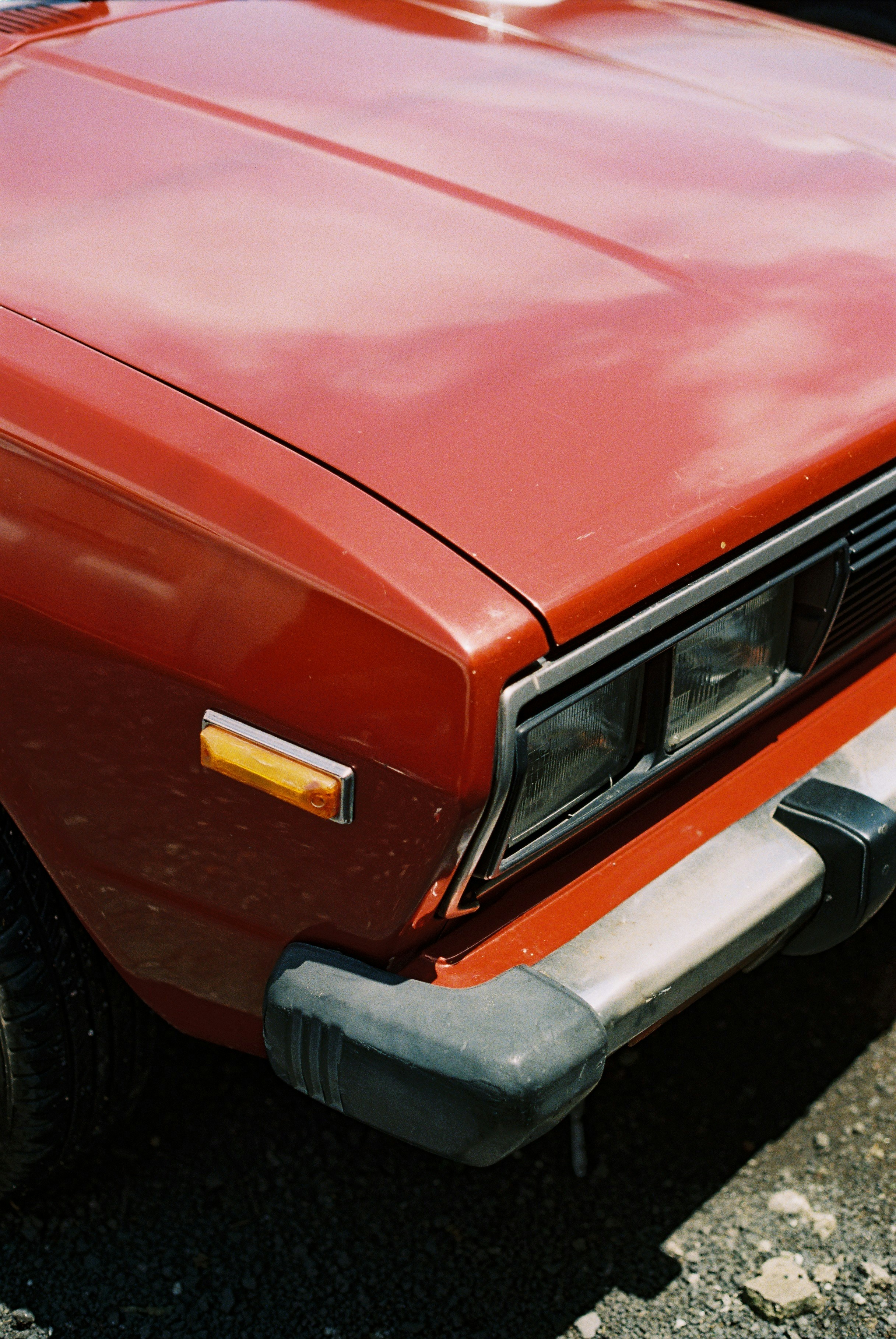 The front corner of a vintage red car with a chrome bumper