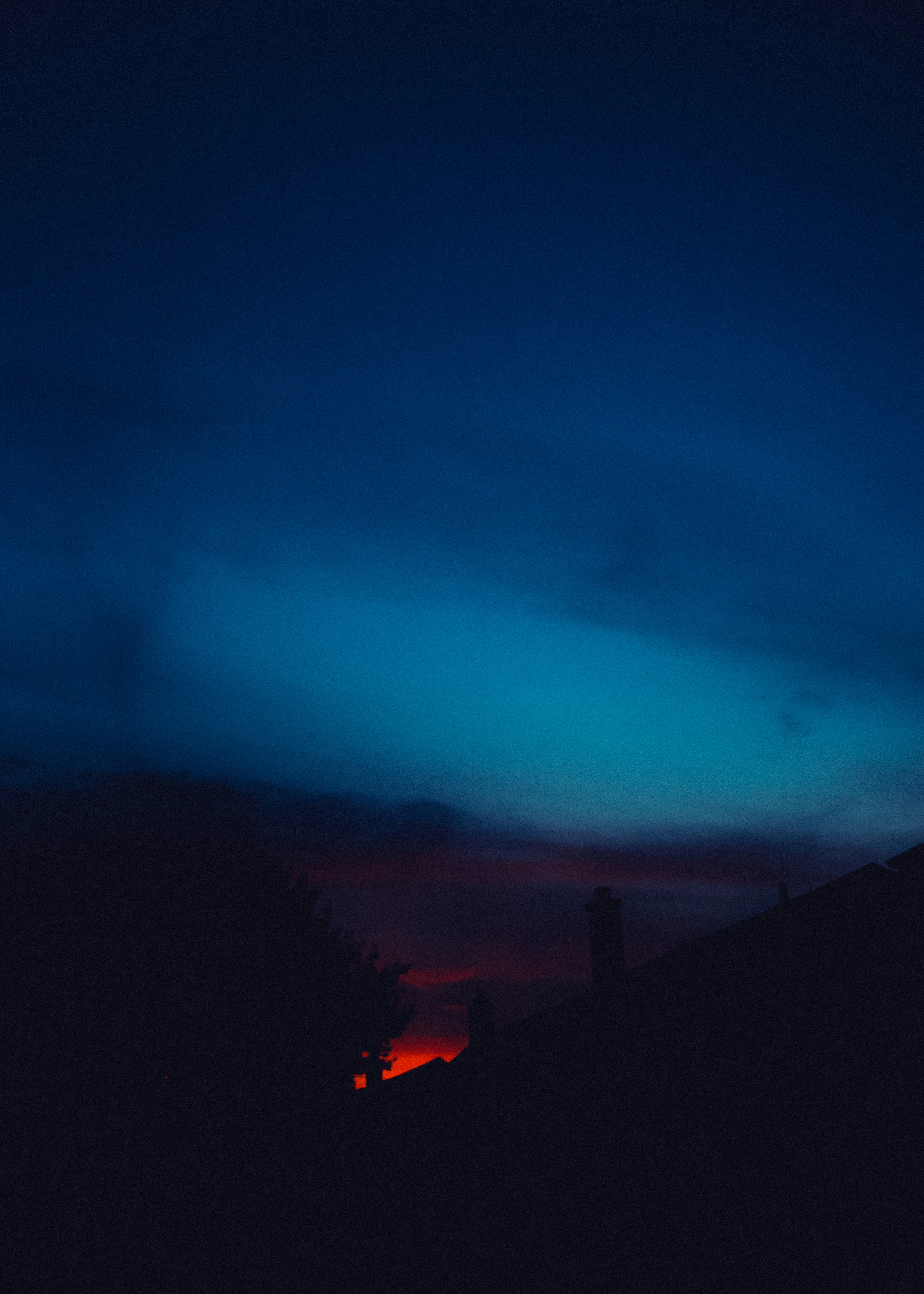 Silhouetted rooftops against a deep blue sky with a glowing orange horizon