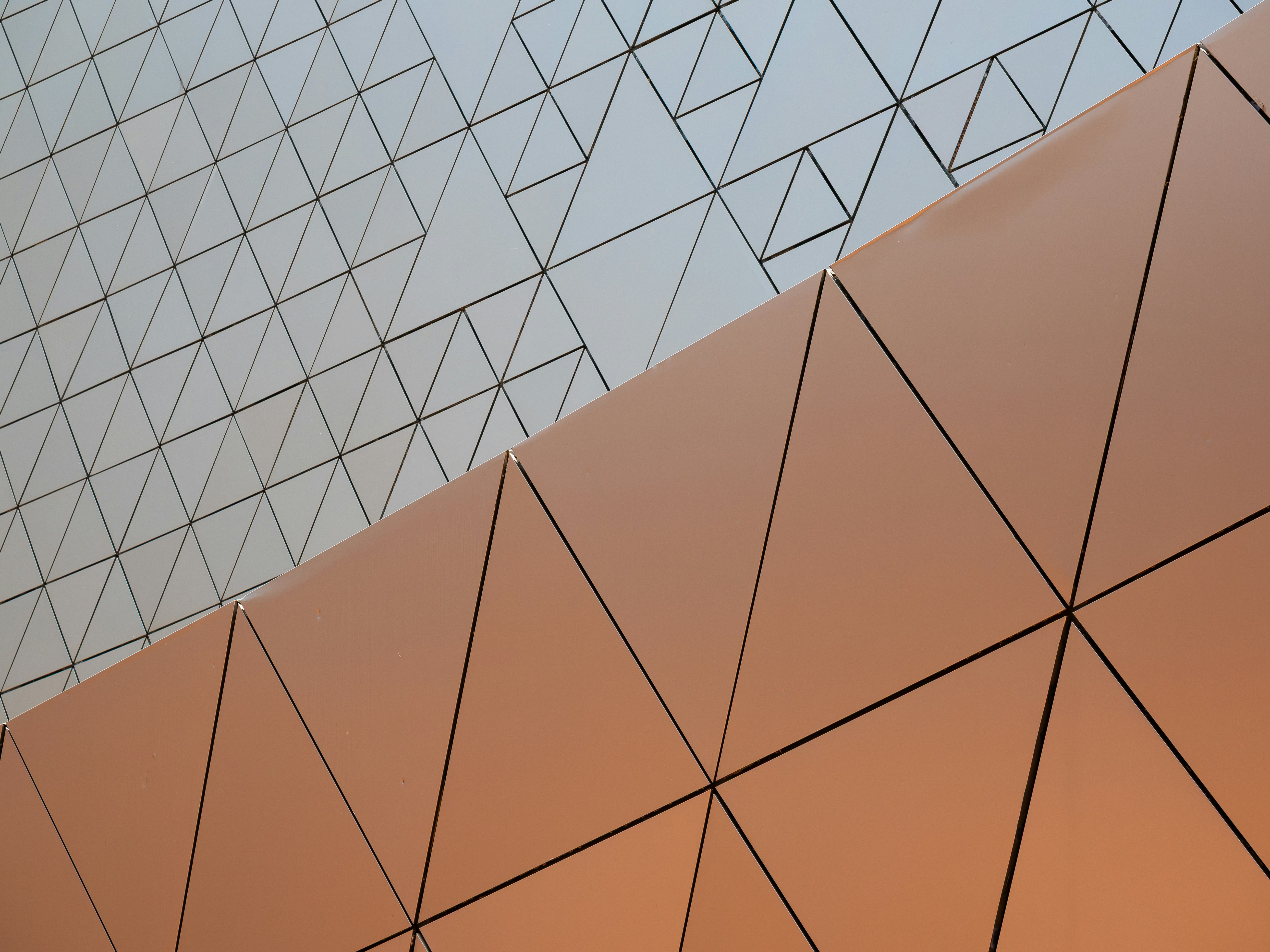 A geometric pattern of copper and white triangular panels on a building facade