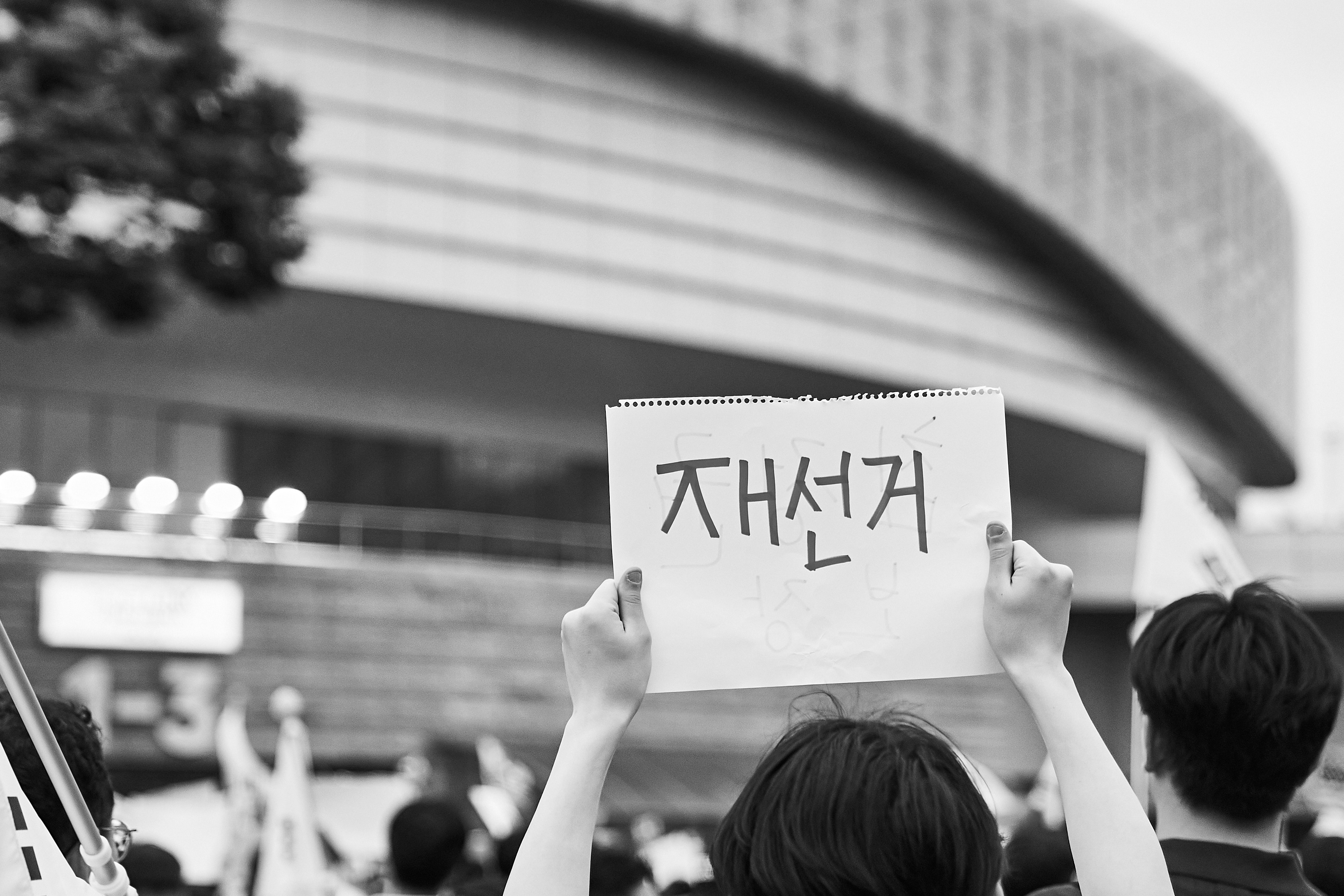 A person holding a sign with Korean text above a crowd at a rally