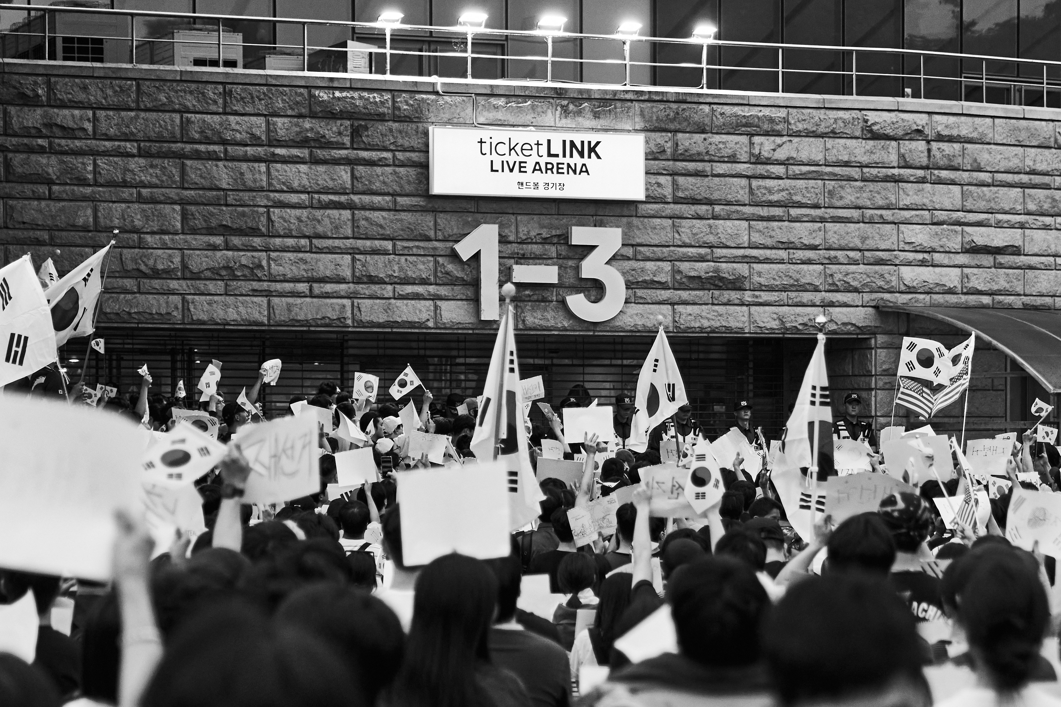 A crowd of people holding South Korean flags and signs outside a stadium