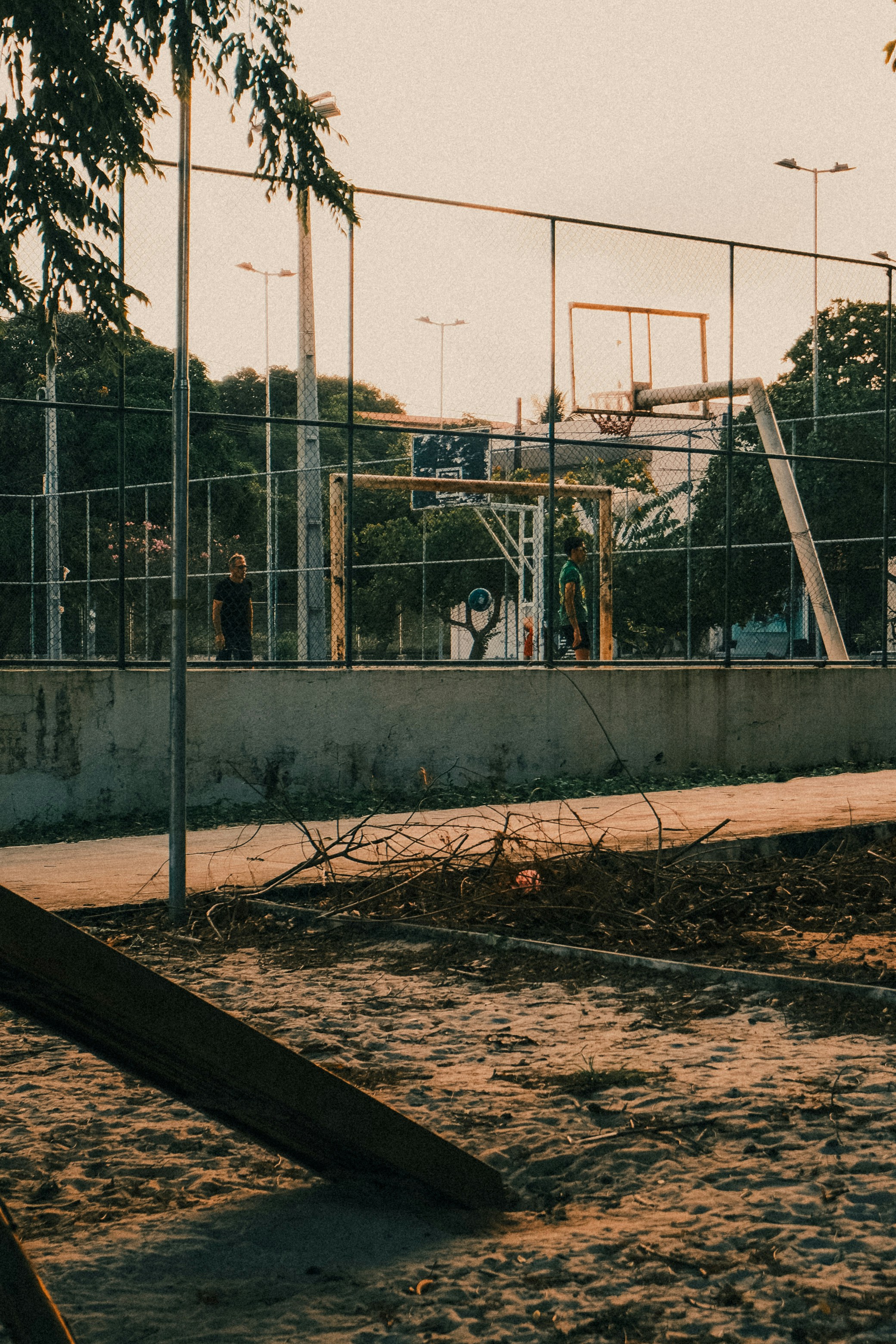 Two people on a fenced basketball court at golden hour
