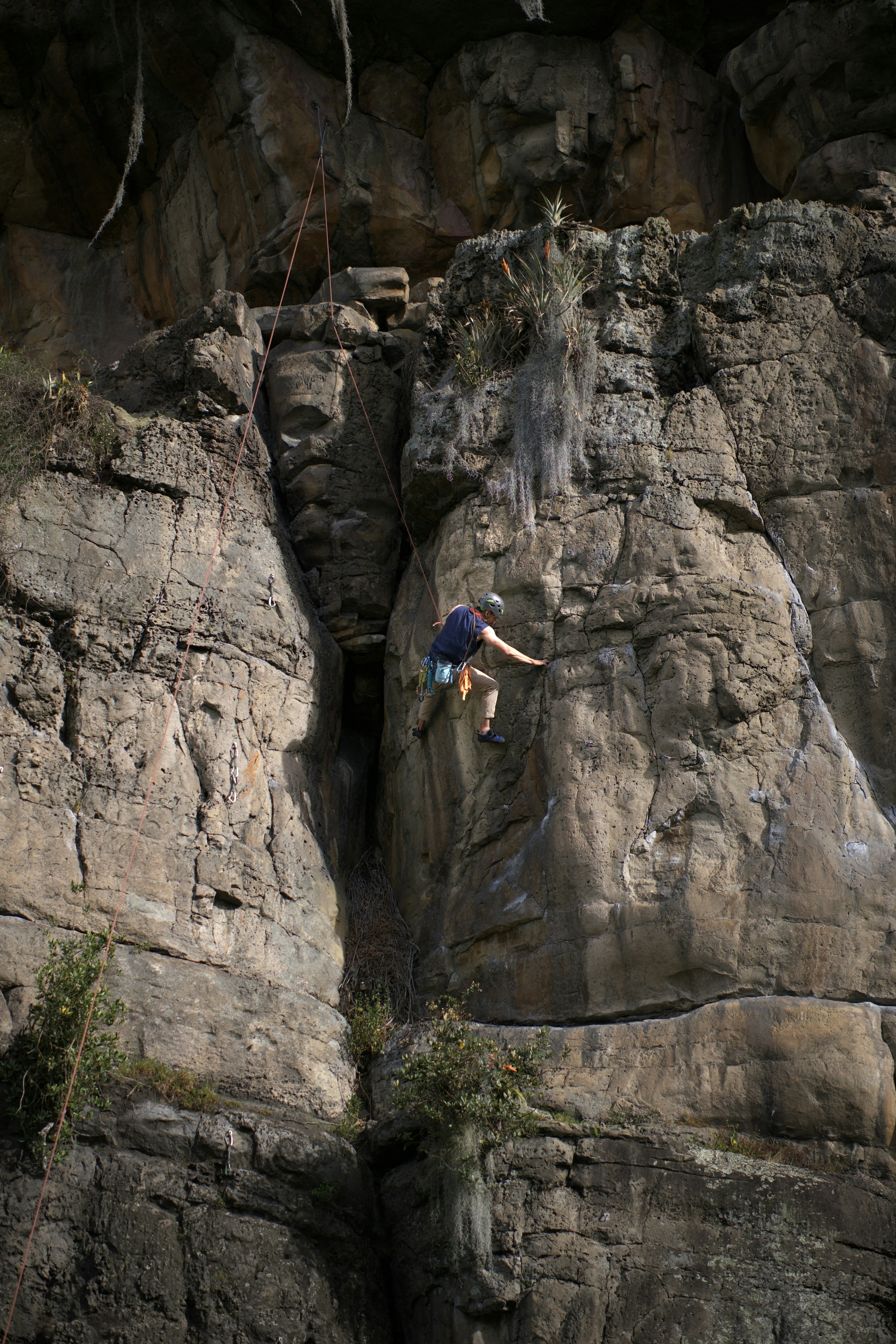 A rock climber scaling a steep textured cliff face with a safety rope