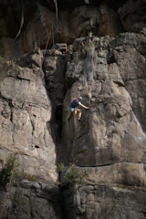 A rock climber scaling a steep textured cliff face with a safety rope