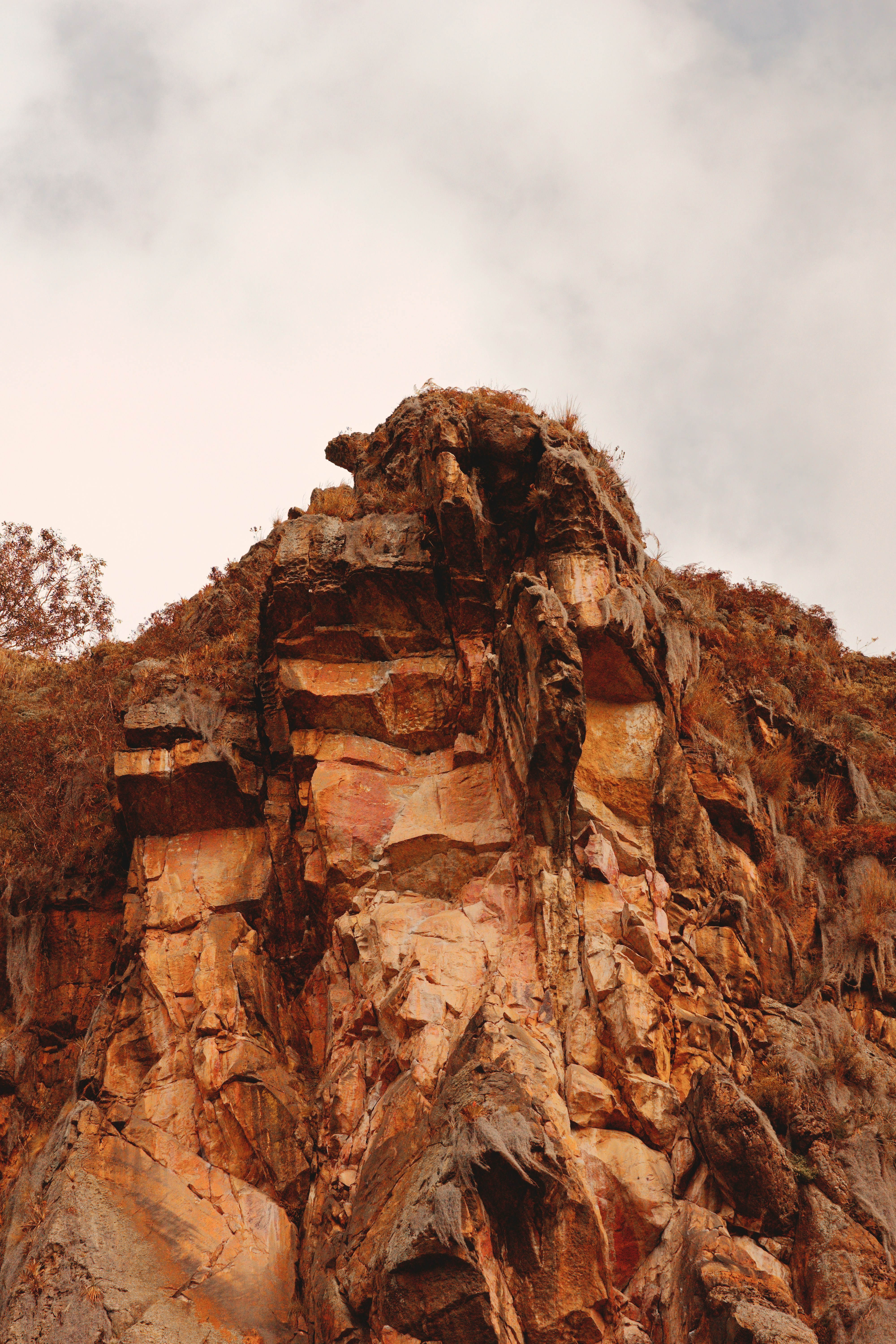 A jagged orange rock formation with sparse vegetation under a cloudy sky