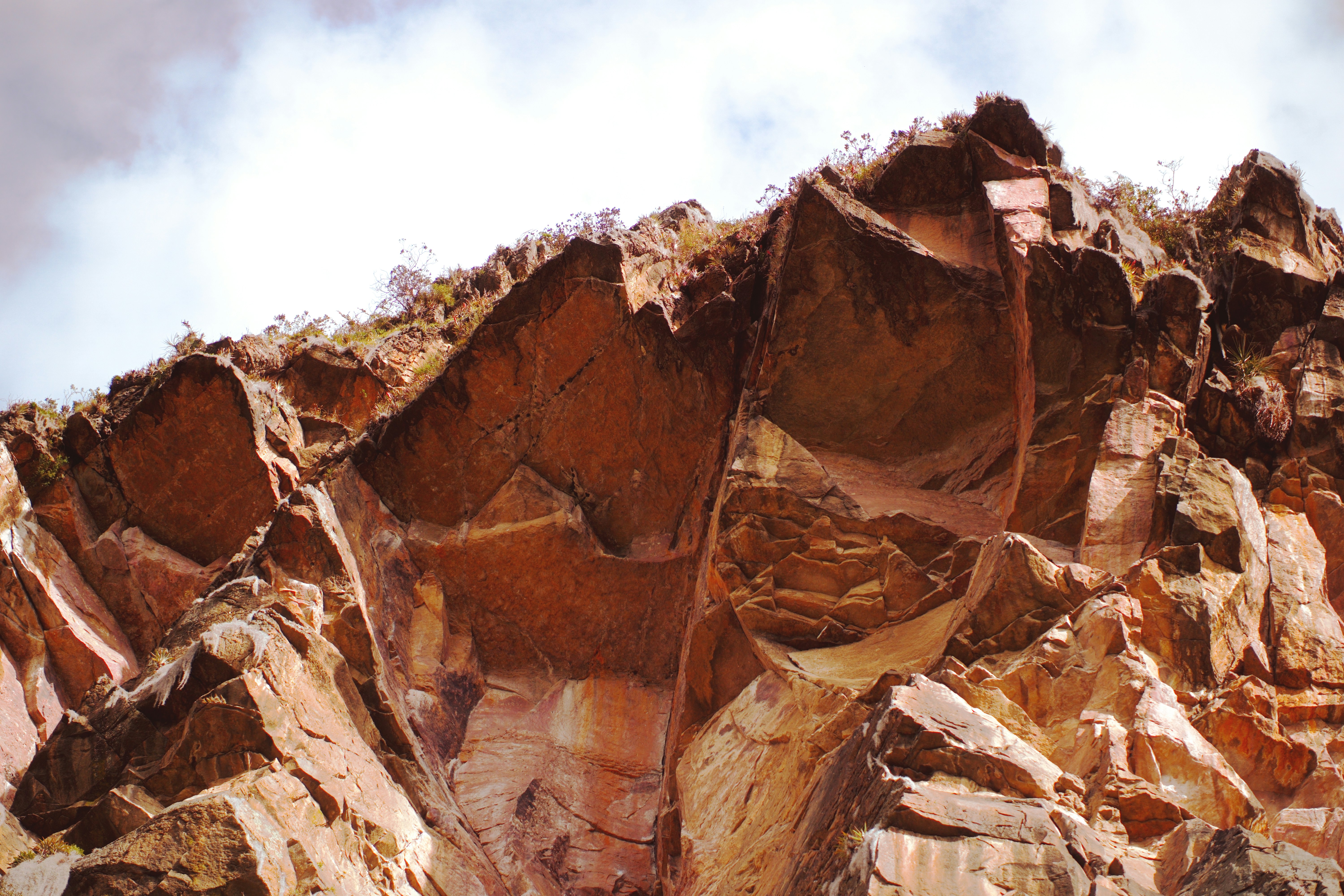 Jagged red rock formations against a cloudy sky with sparse vegetation
