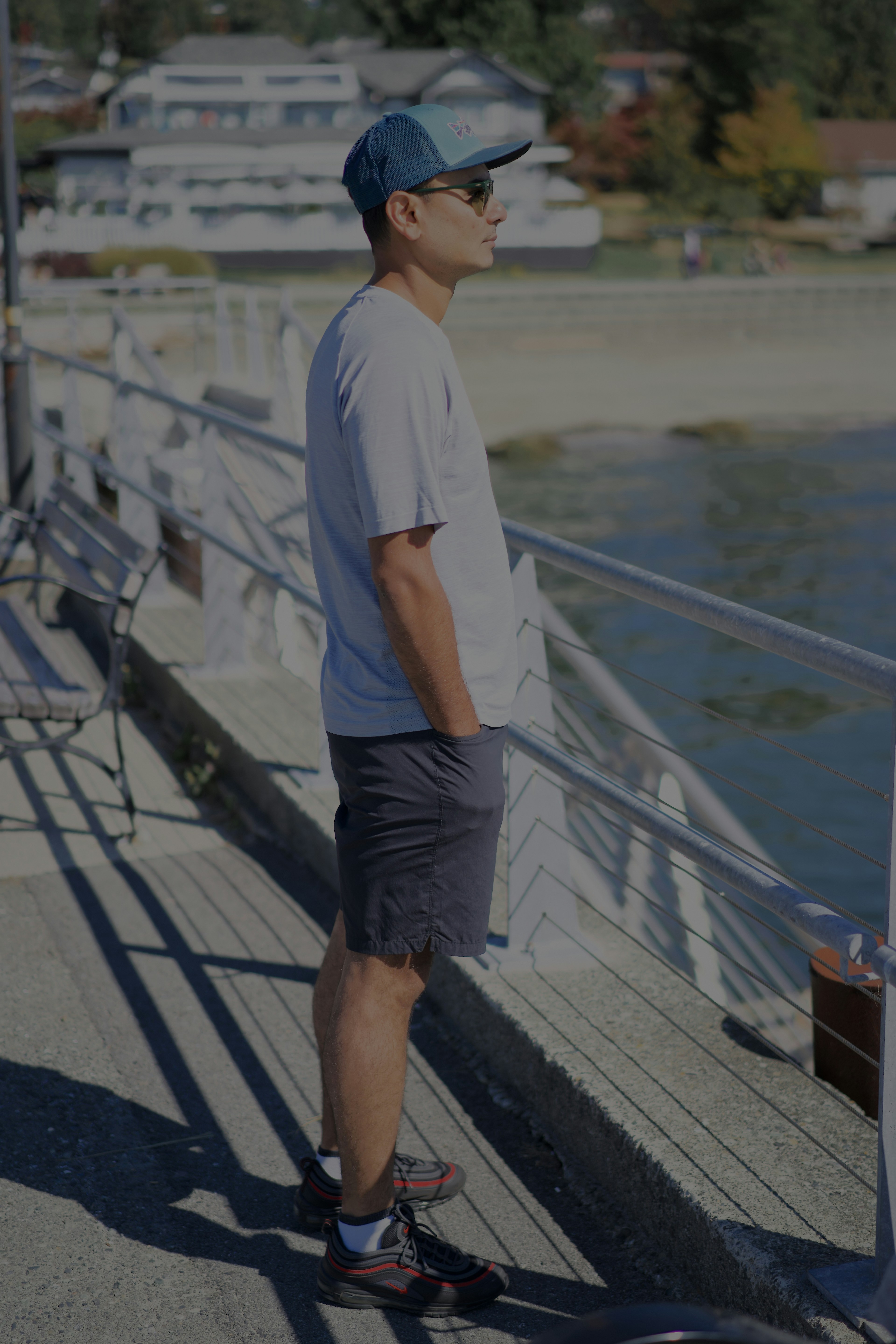 A man in a baseball cap and t-shirt standing by a metal railing