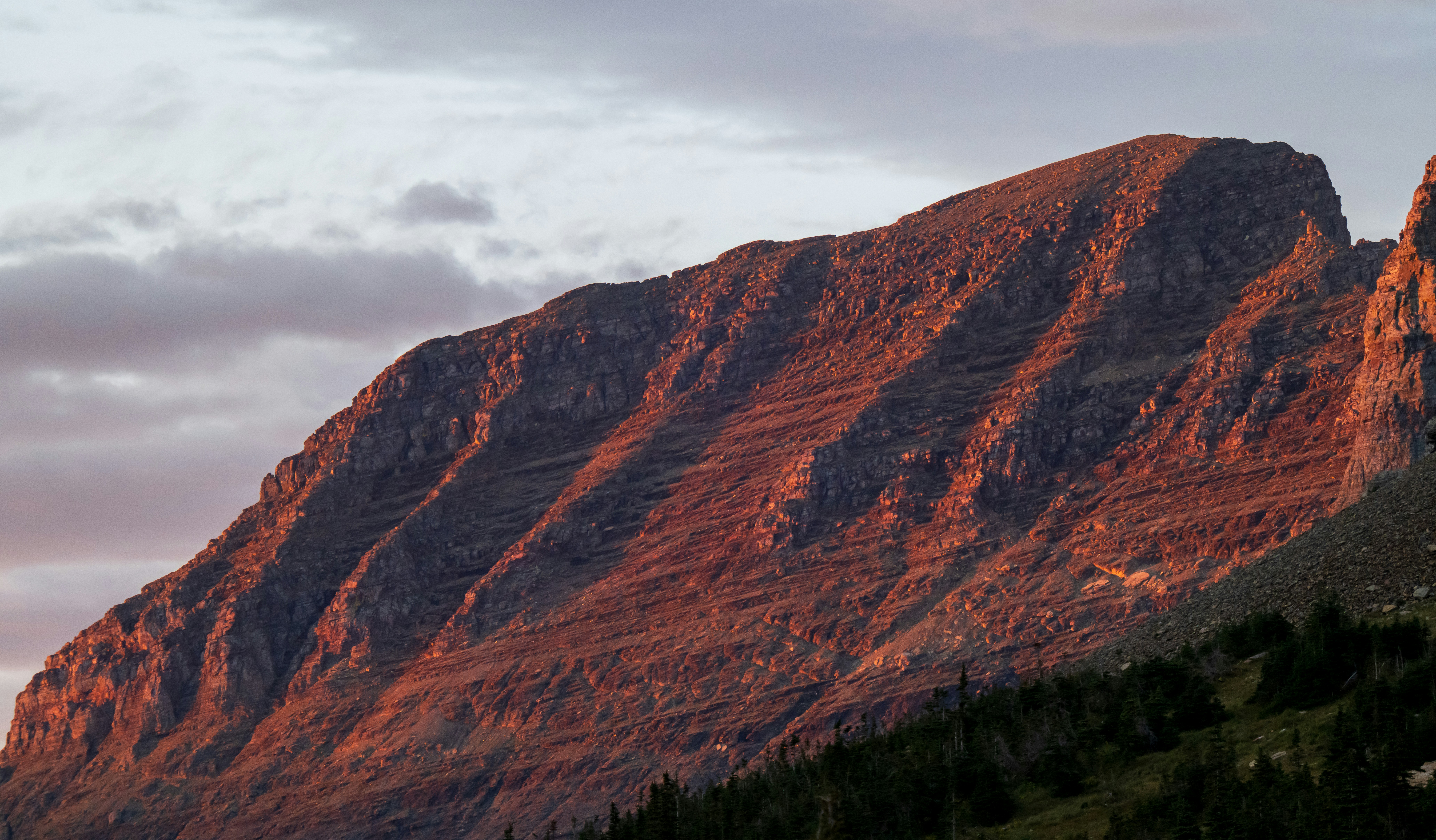 A rocky mountain peak illuminated by warm light against a cloudy sky