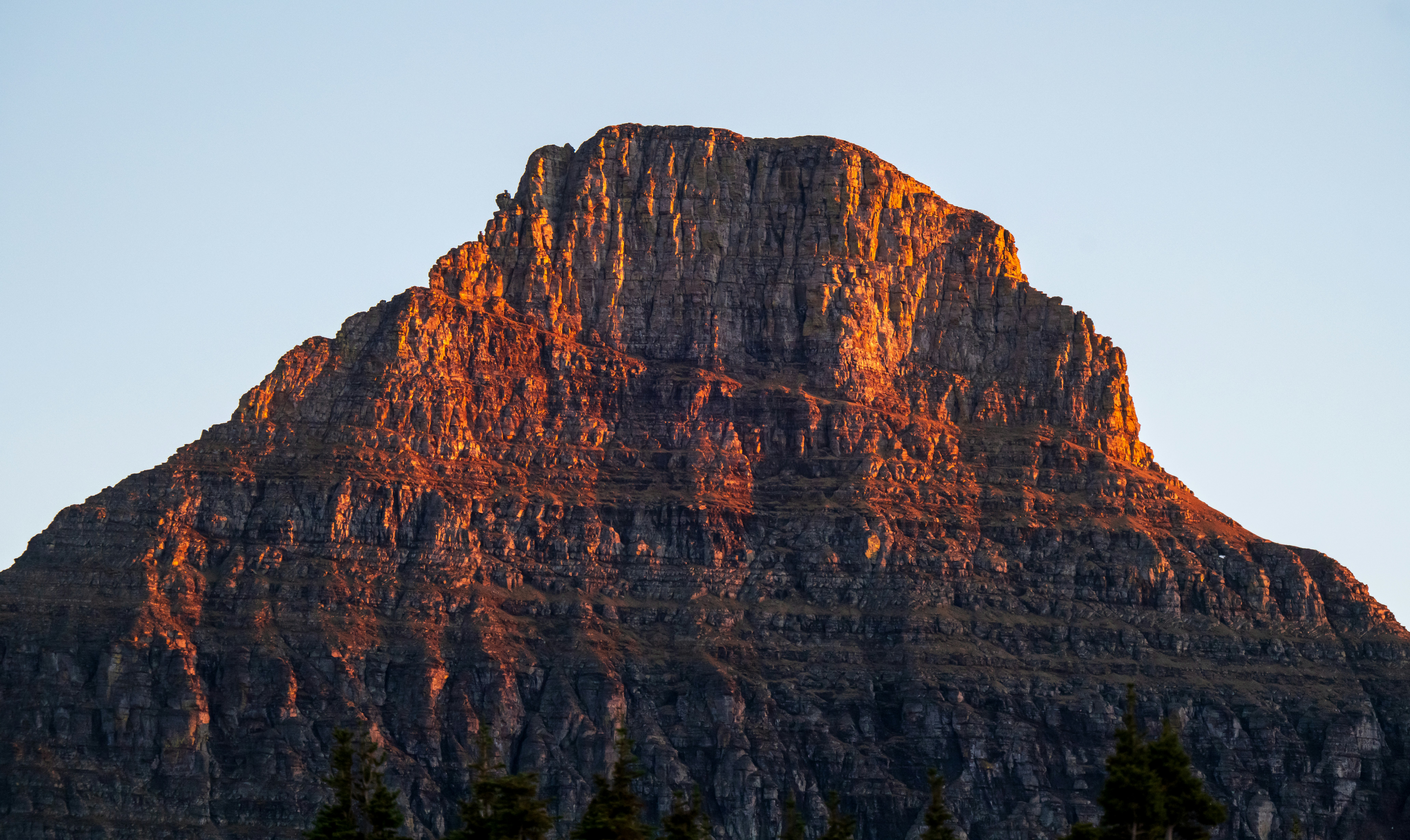 A rocky mountain peak illuminated by warm golden light against a clear sky