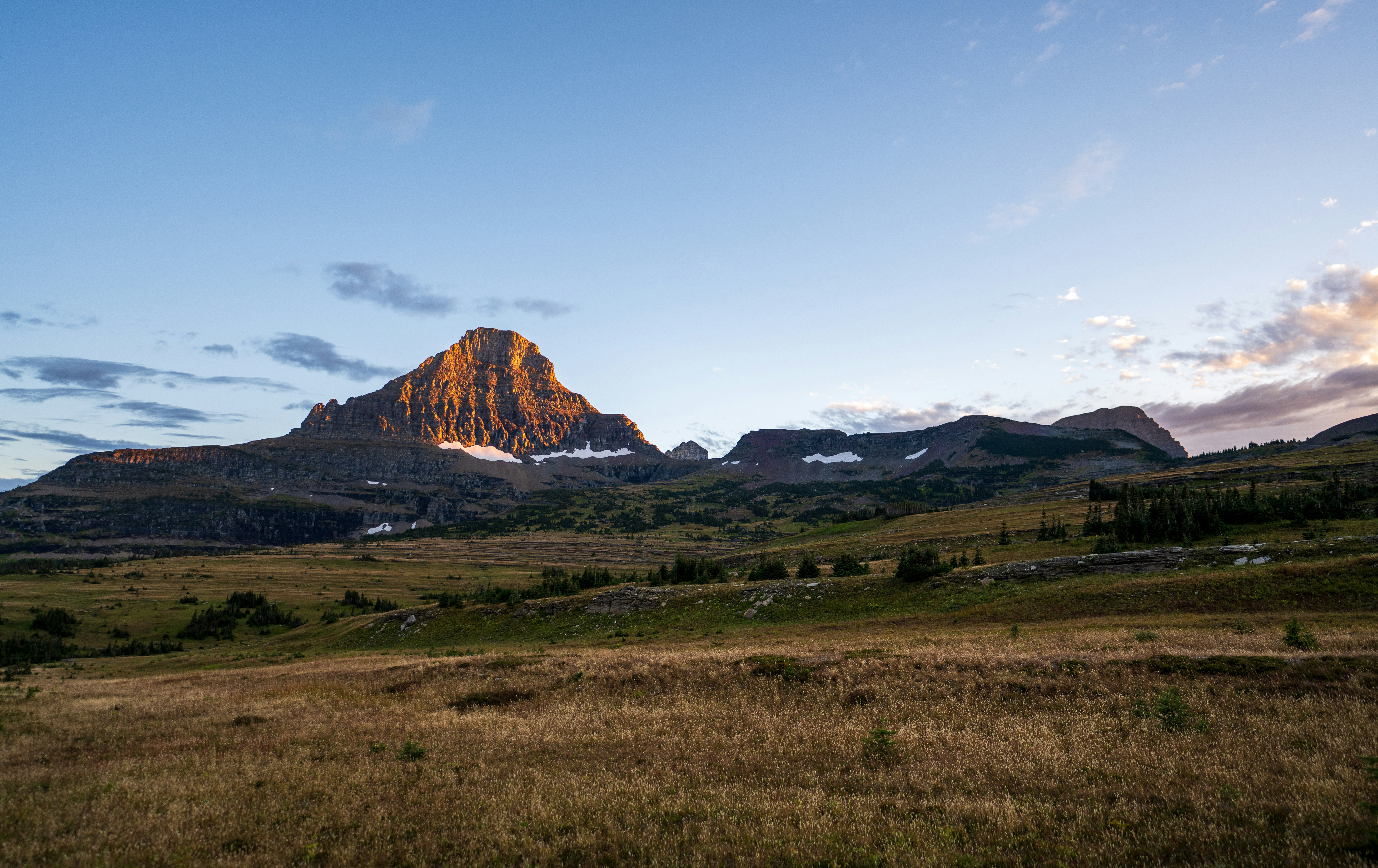 A mountain peak illuminated by golden light above a vast grassy alpine meadow
