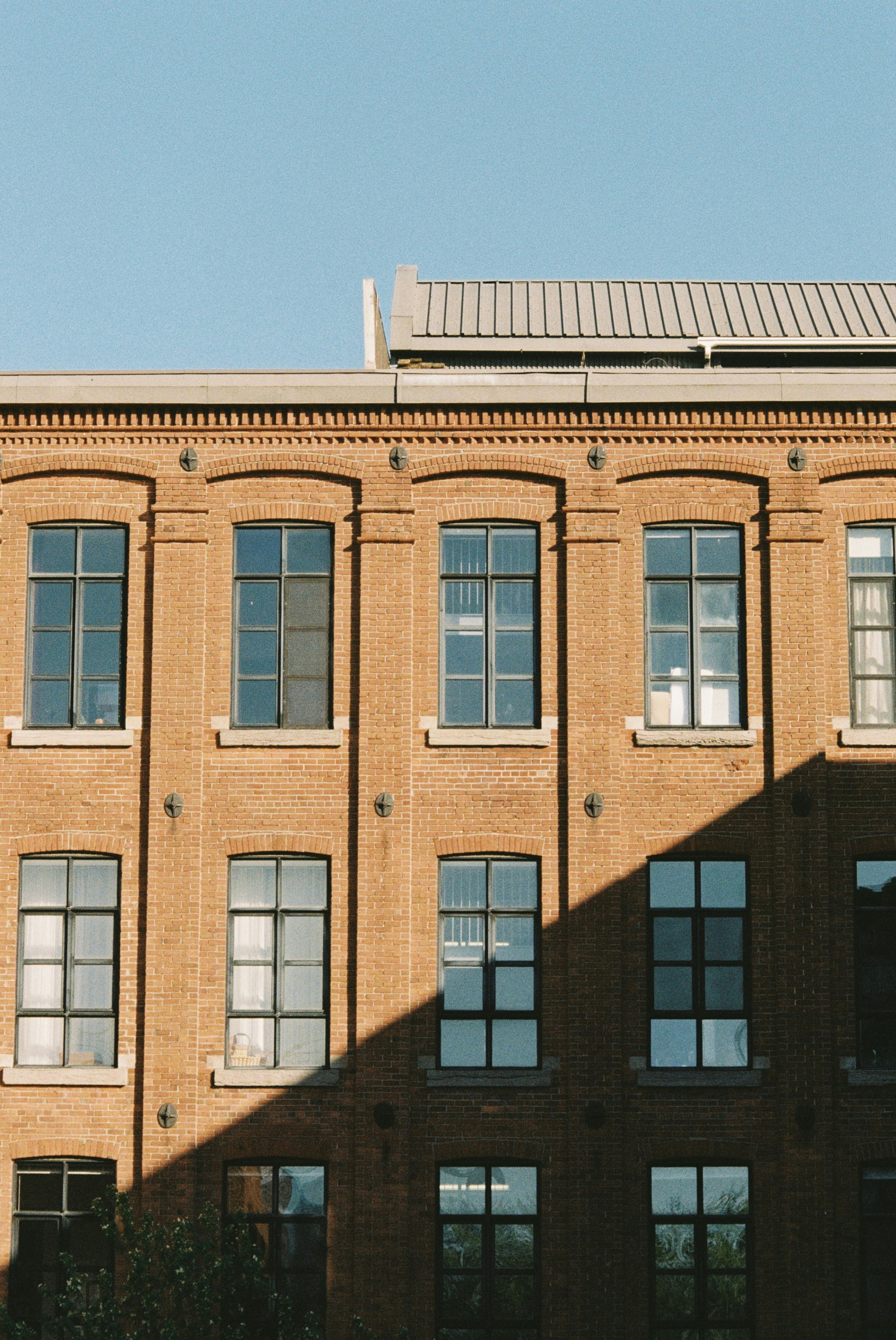 Photo of A red brick building facade with grid windows and a sharp diagonal shadow by Julie Gaïa Guzal