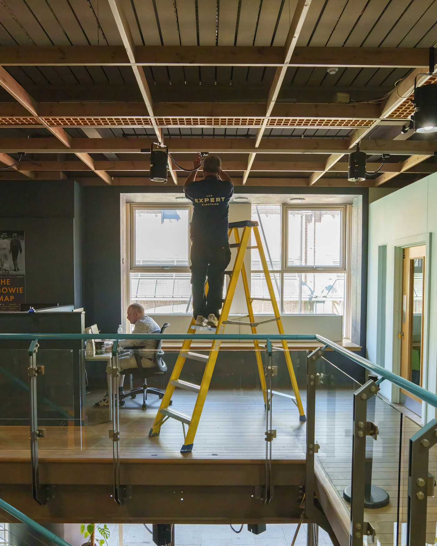 Electrician on a ladder fitting ceiling lights in an office