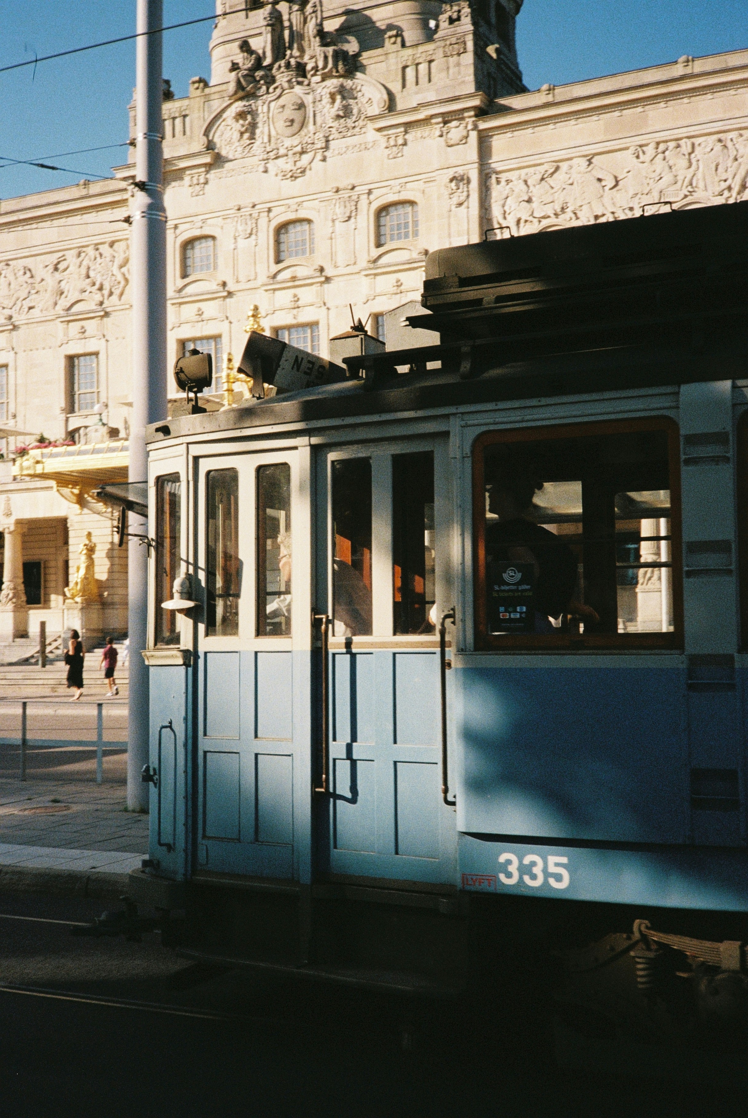 A vintage blue tram car passing an ornate stone building in Stockholm