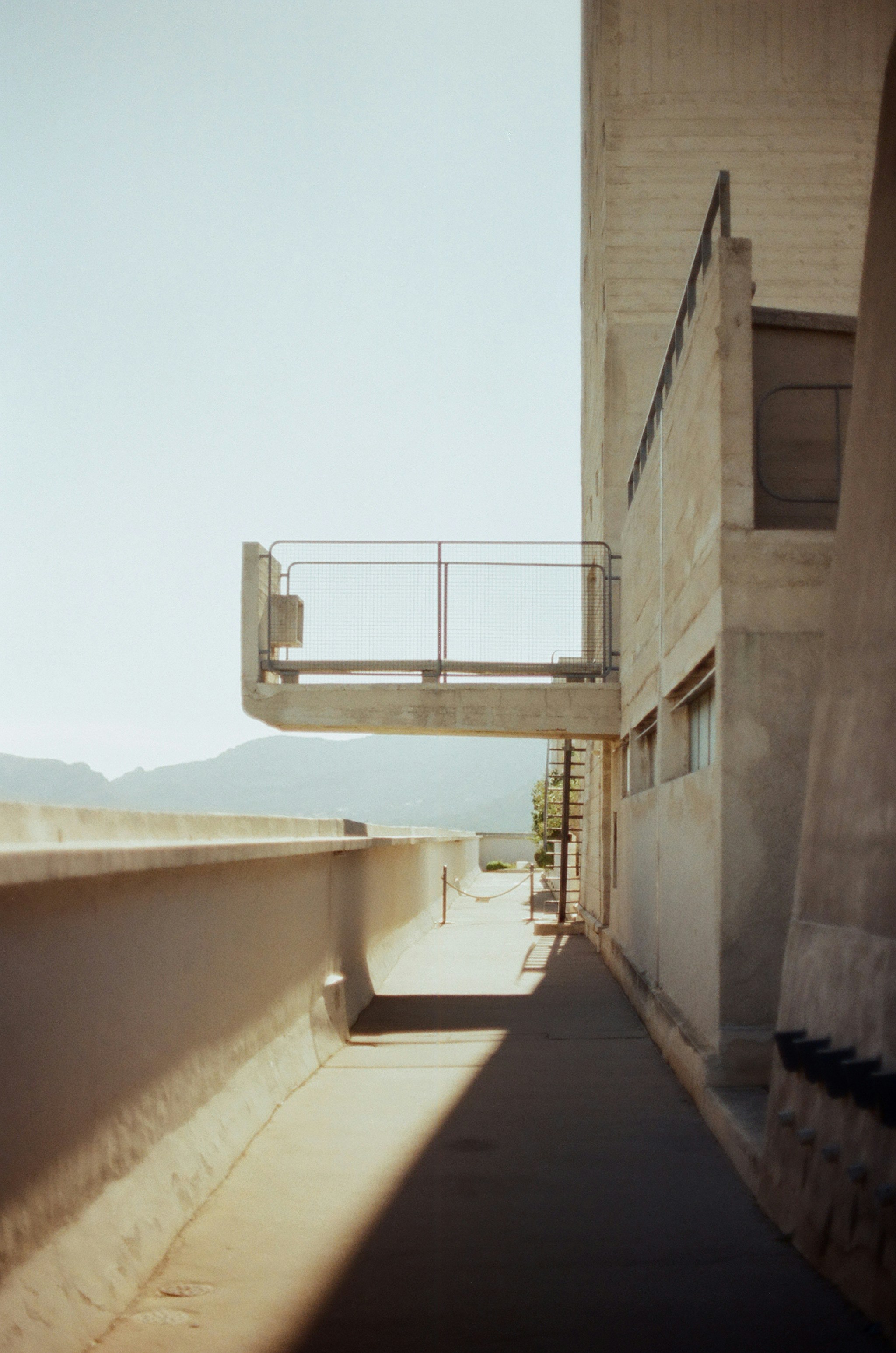 A concrete walkway with a cantilevered balcony overlooking distant mountains in bright light