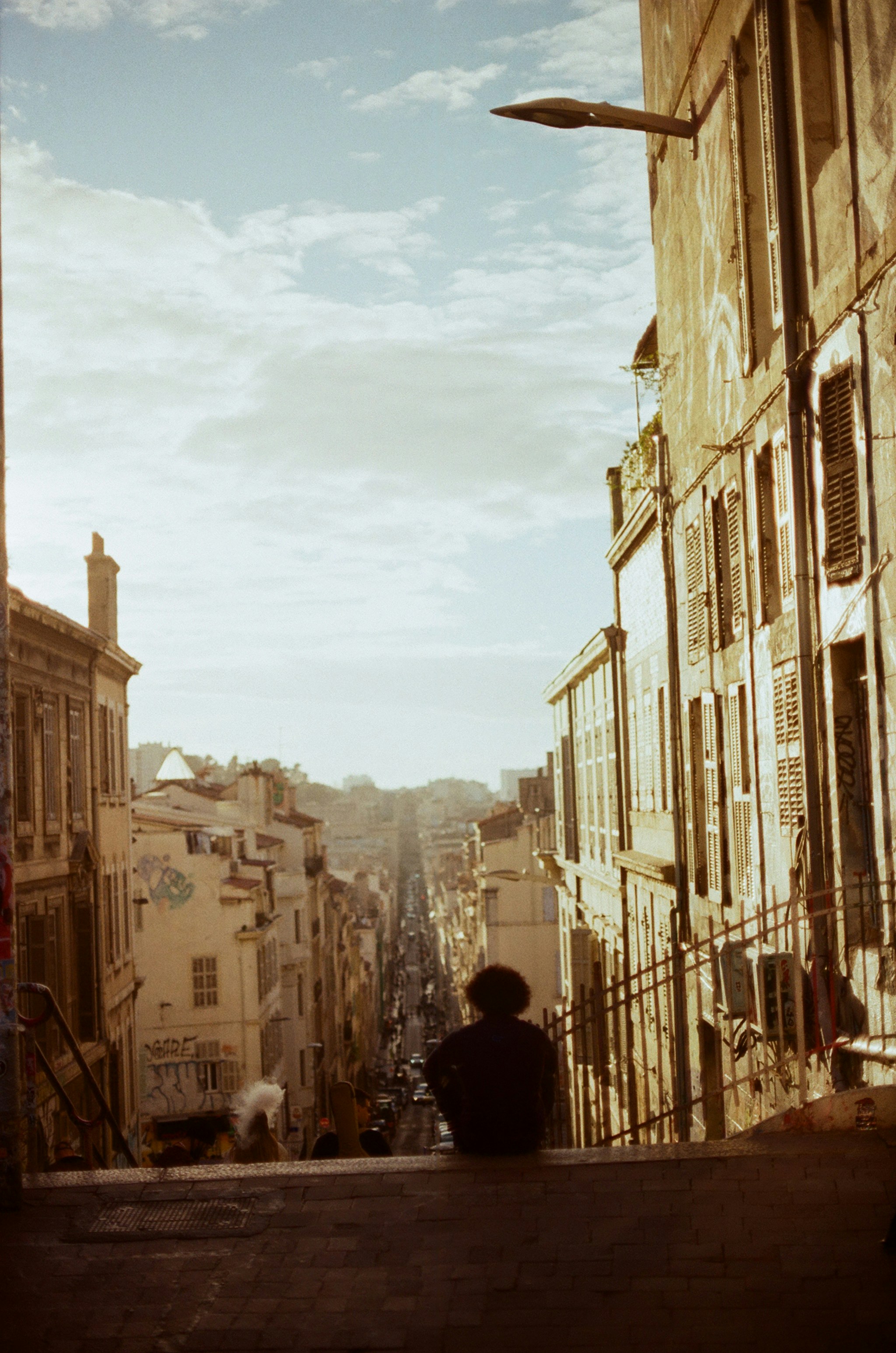 A person with curly hair sitting on a ledge overlooking a narrow city street