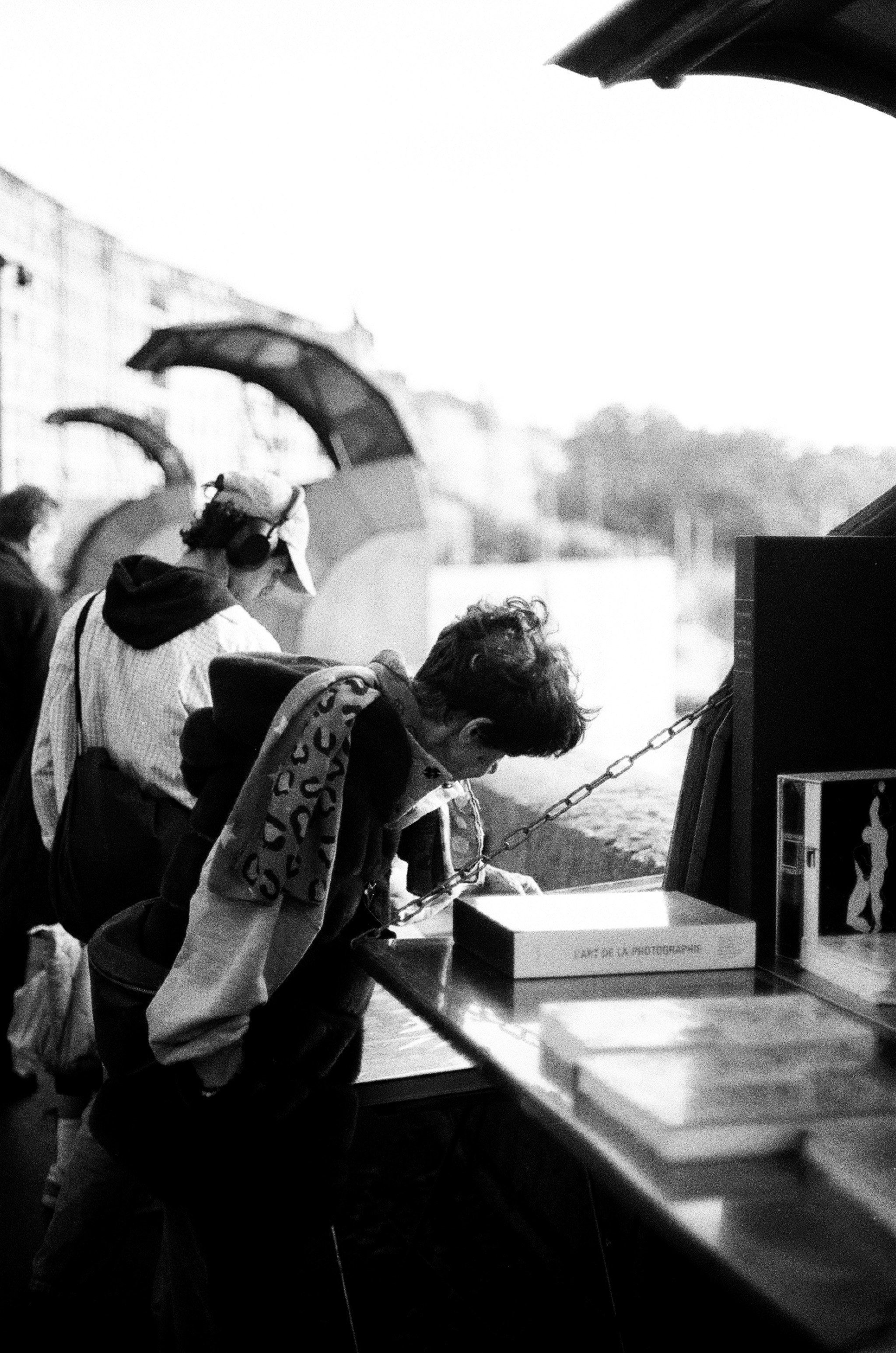 Two people browsing books at an outdoor stall in black and white