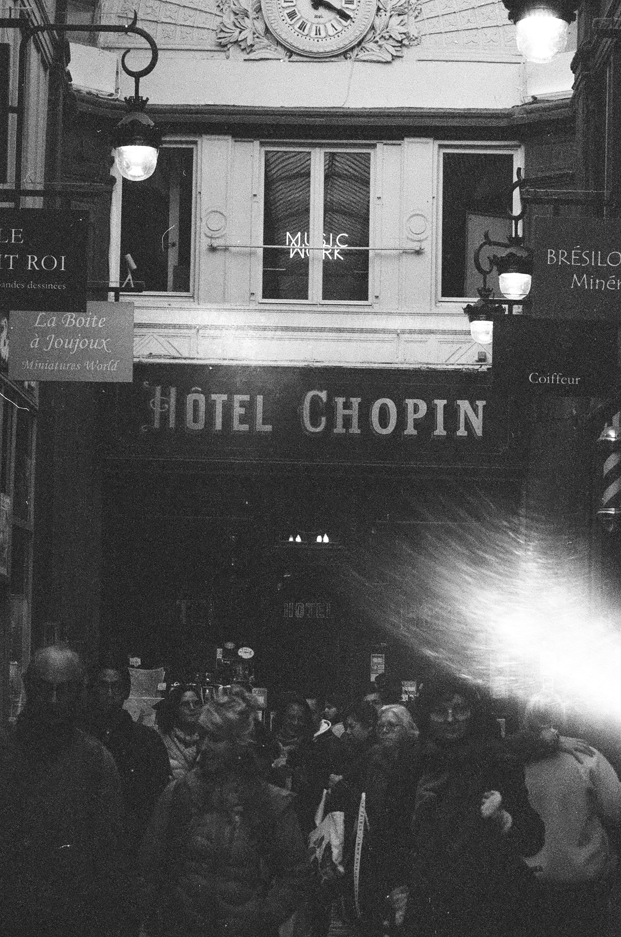 A crowd of people walking past the Hotel Chopin in a Parisian arcade
