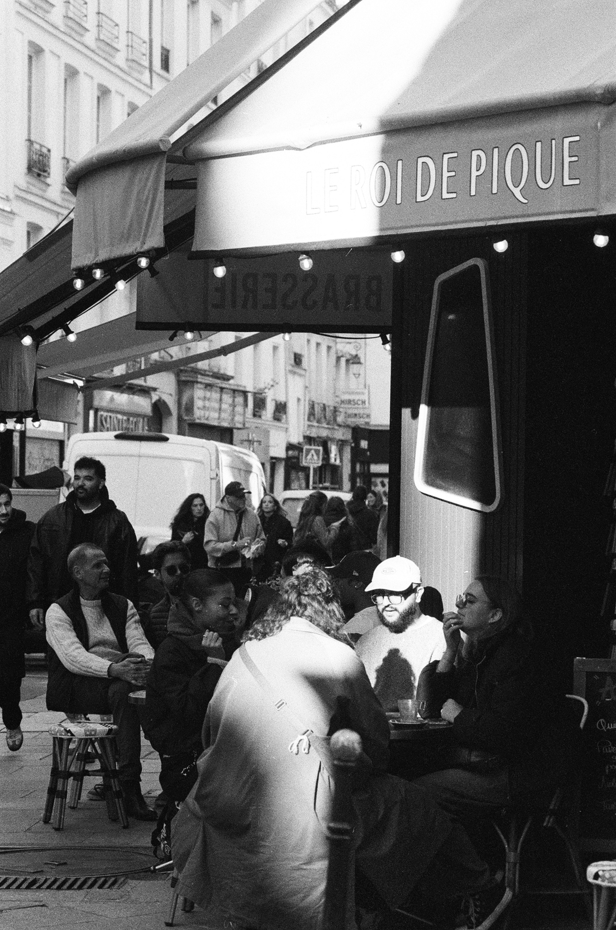 People sitting at tables outside a brasserie named Le Roi de Pique in Paris