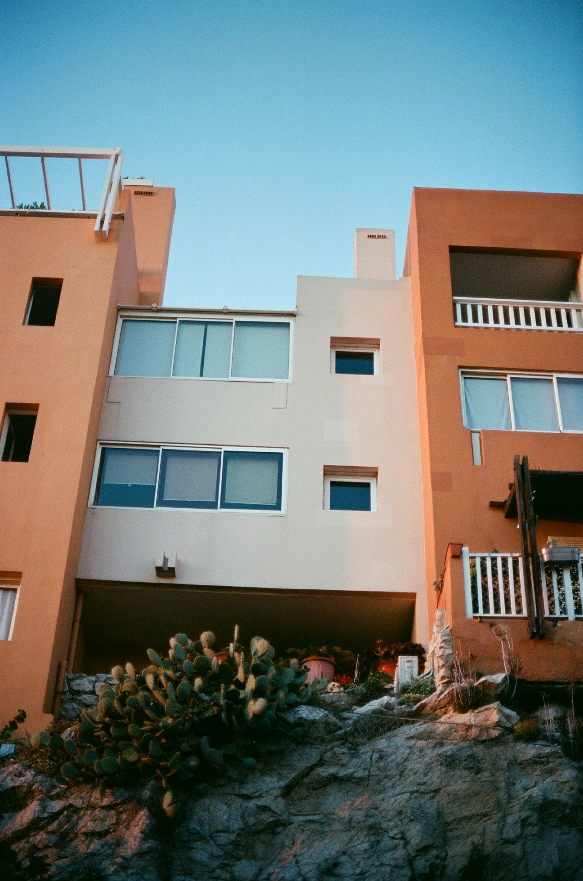 A multi-story apartment building with orange and cream walls above a rocky cactus garden
