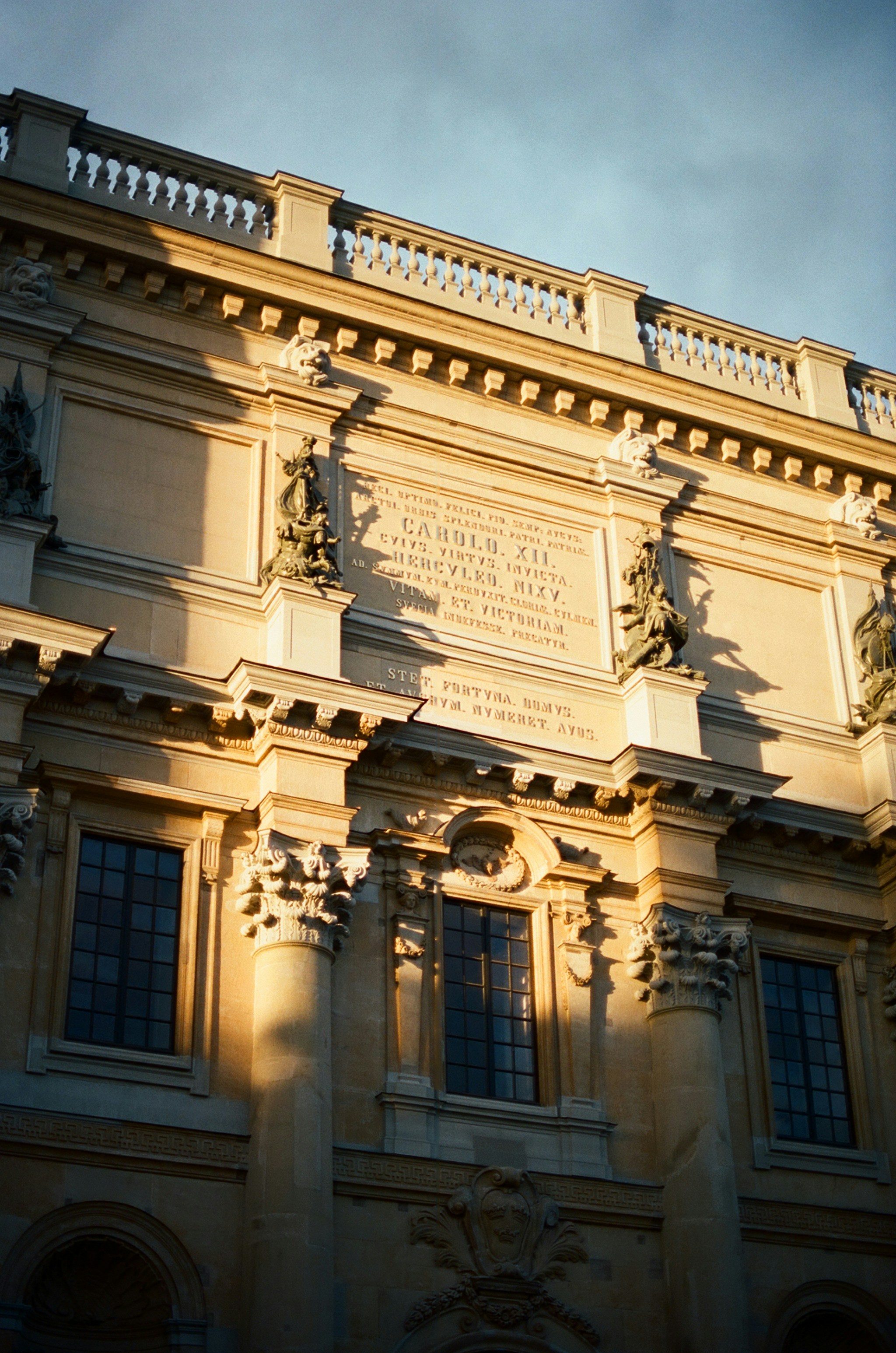 Classical stone facade with Latin inscriptions and ornate sculptures in warm golden hour light