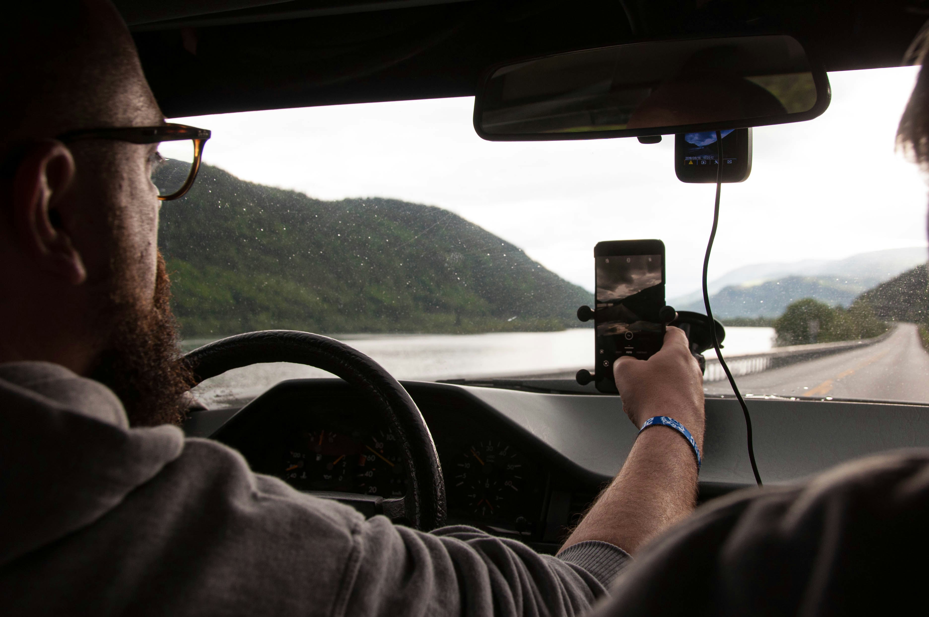 A person driving a car while holding a smartphone to record the road