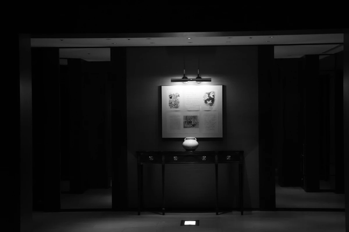 Moody modern interior hallway with dark cabinetry, recessed doorways, a central console, framed artwork and focused architectural lighting.