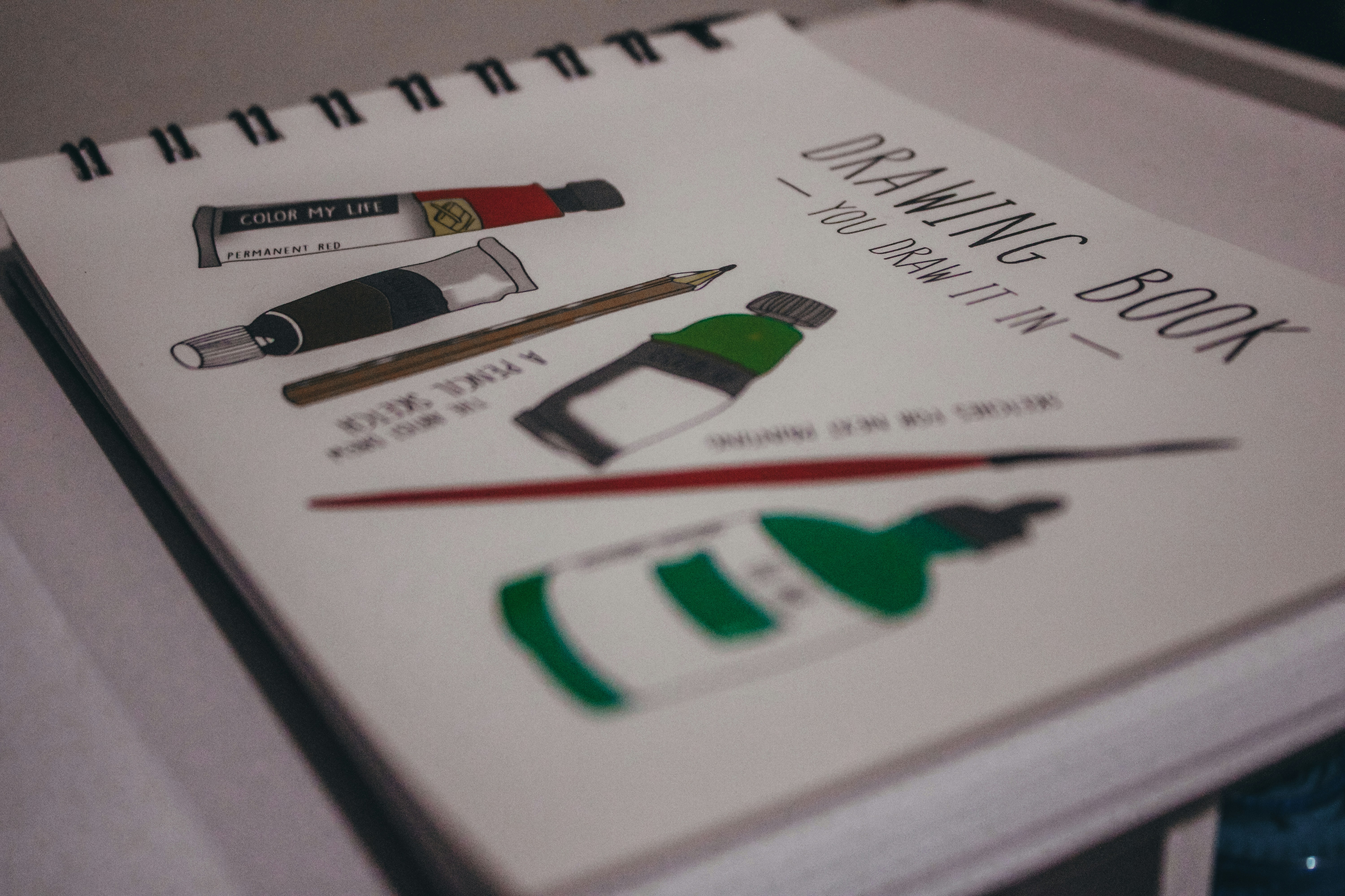 A drawing book with illustrations of paint tubes, a pencil, and a brush