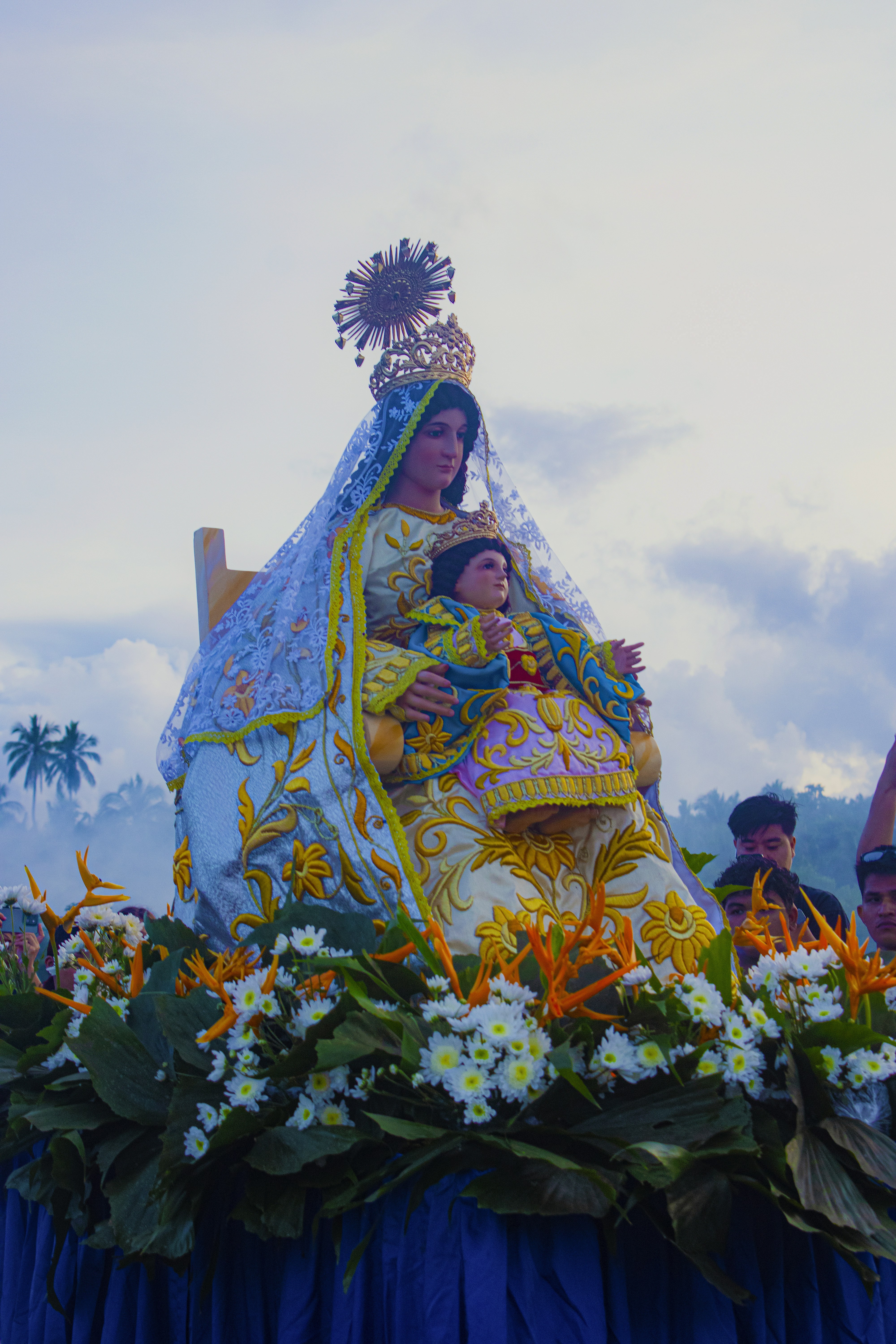 A statue of the Virgin Mary and child Jesus decorated with flowers in procession