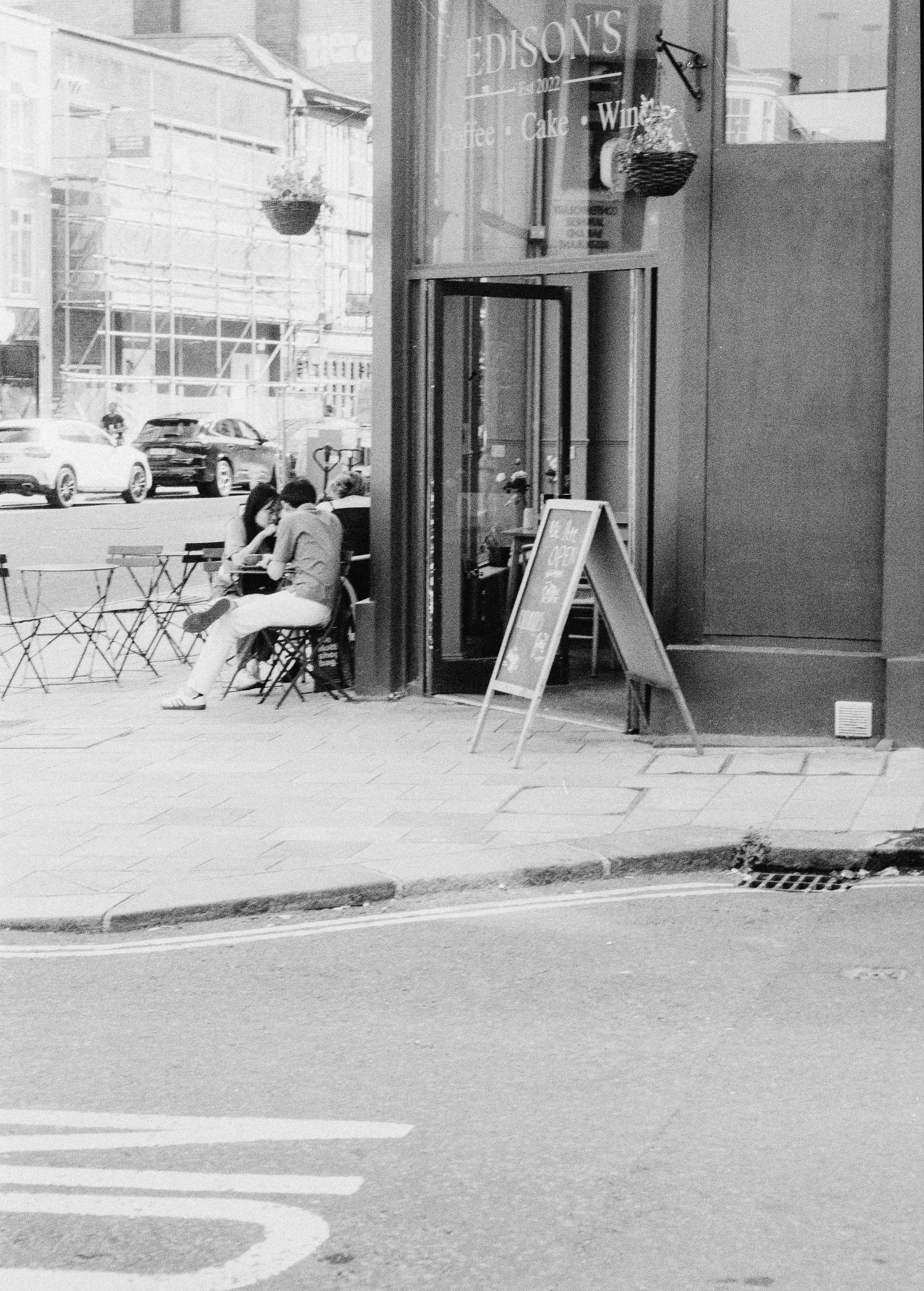 Two people sitting at a small table outside a cafe with an open sign