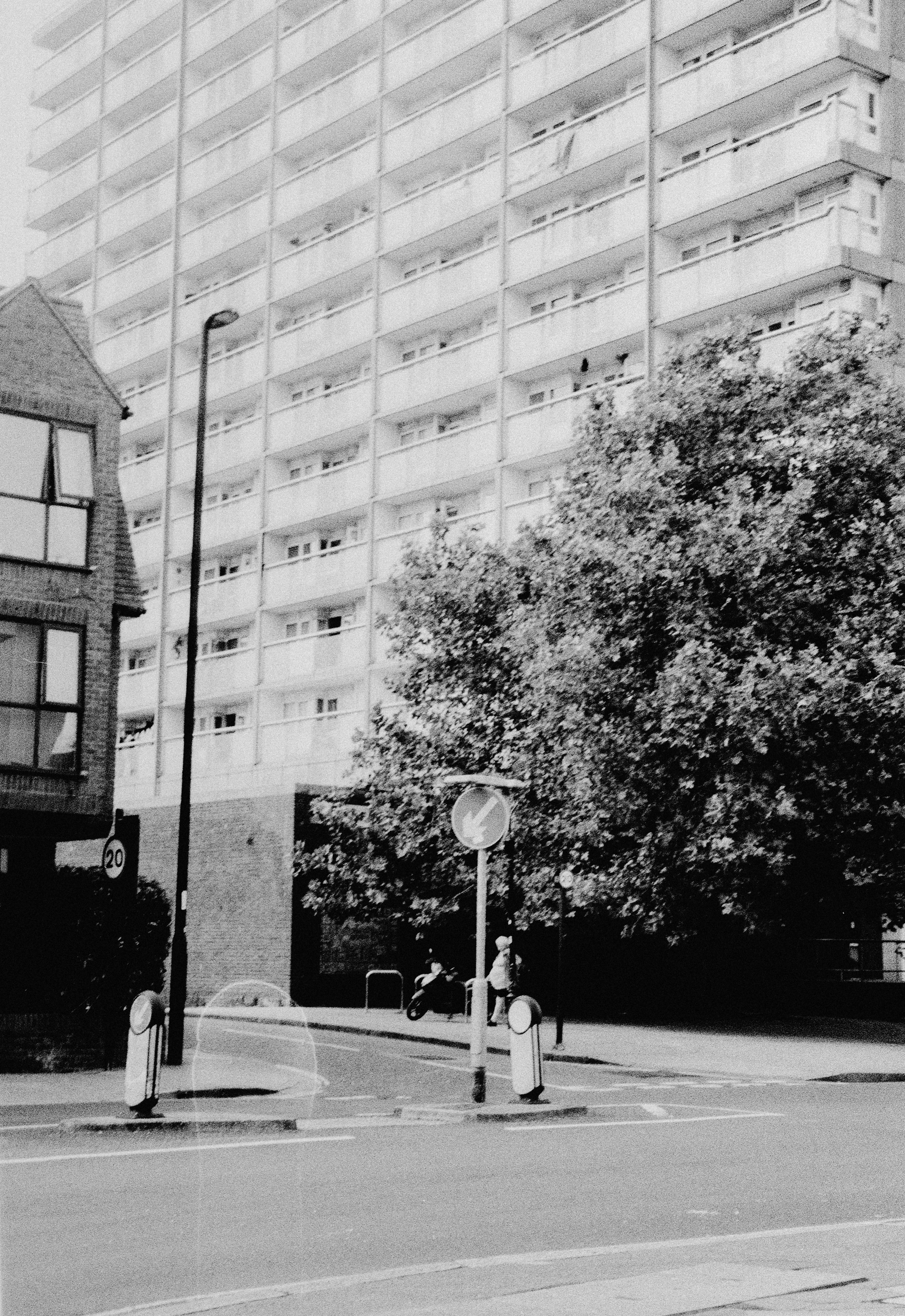 A tall apartment building behind a street with a traffic sign and tree
