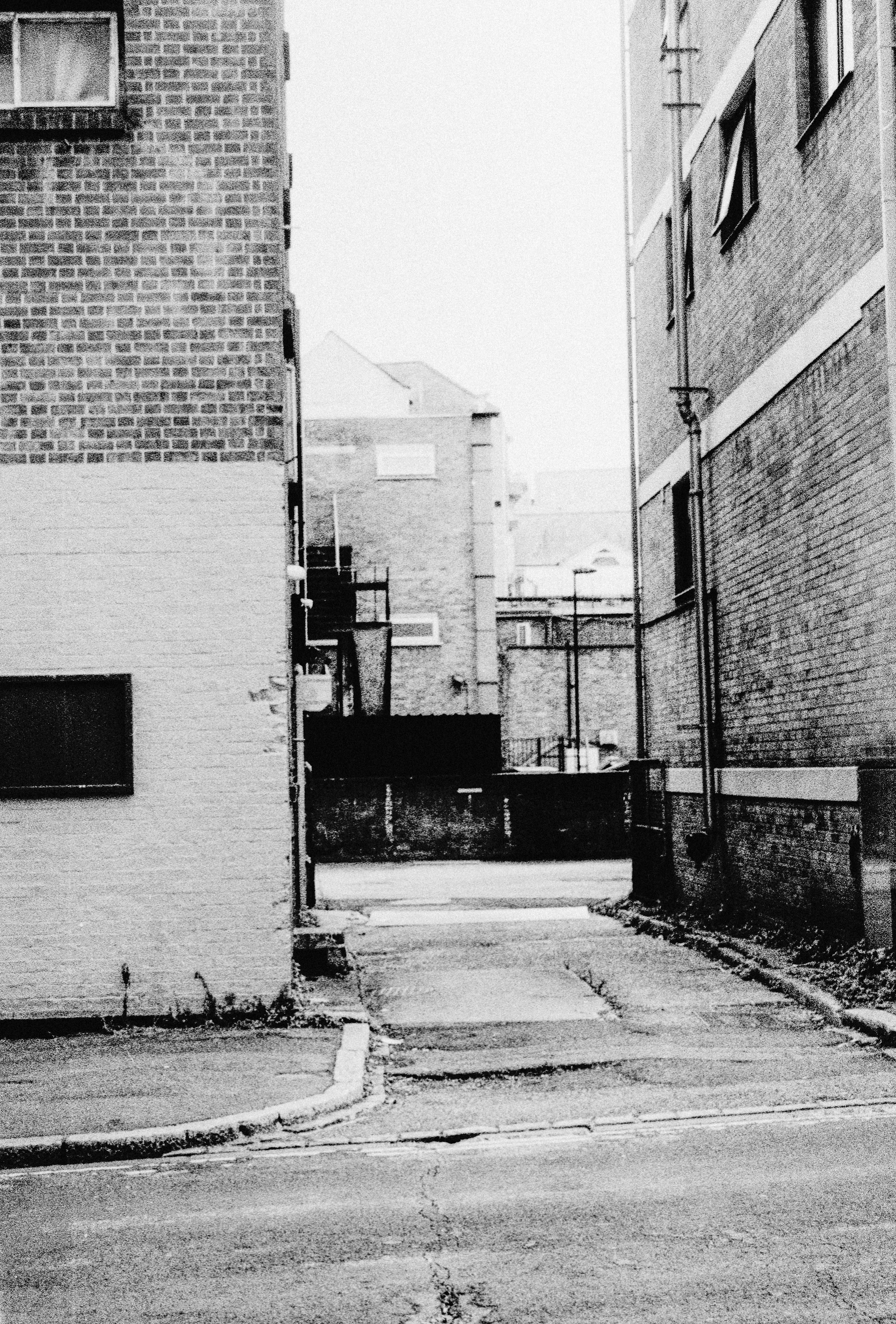 A narrow alleyway between two brick buildings leading to a paved courtyard