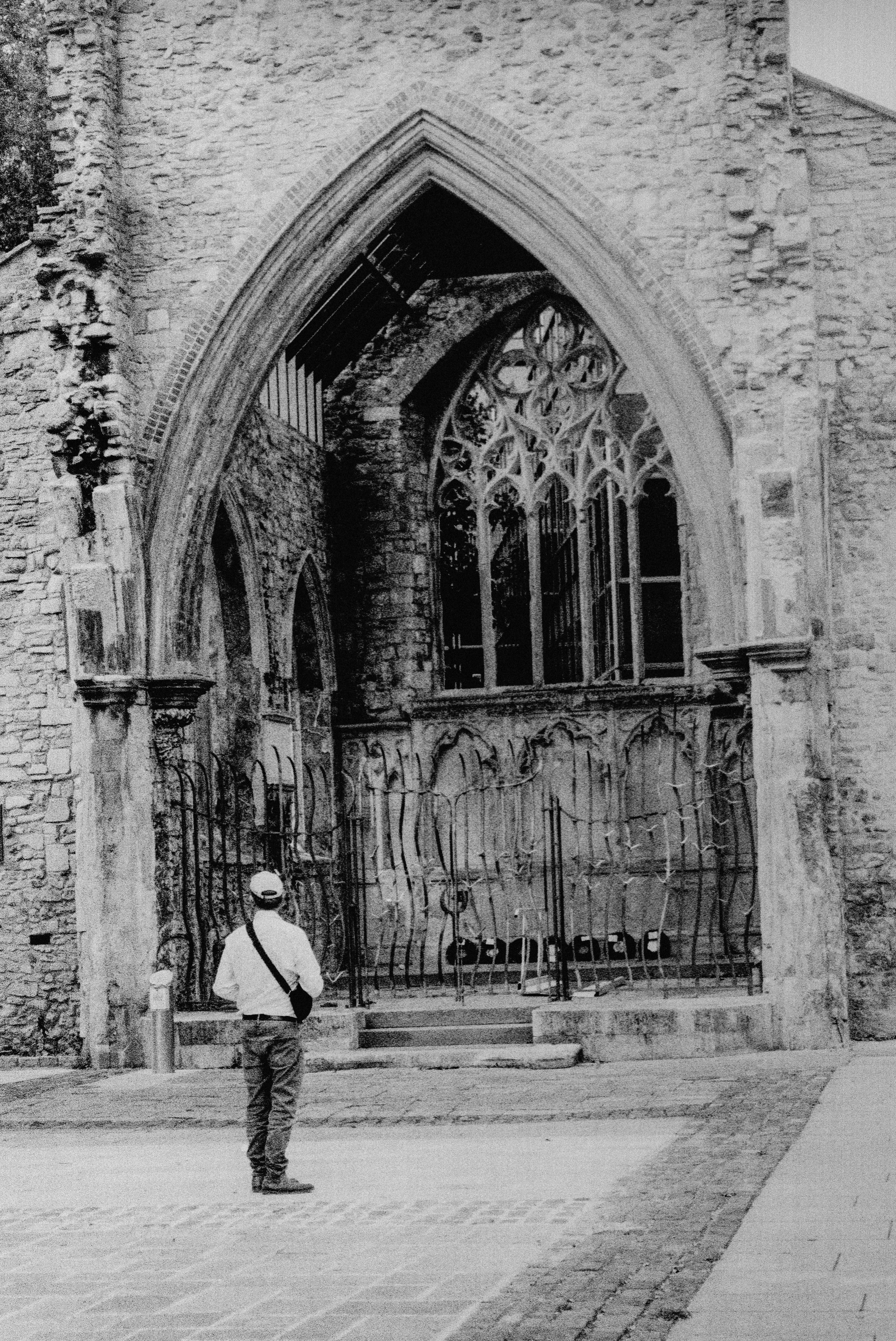 A person in a white shirt and jeans facing a stone gothic archway