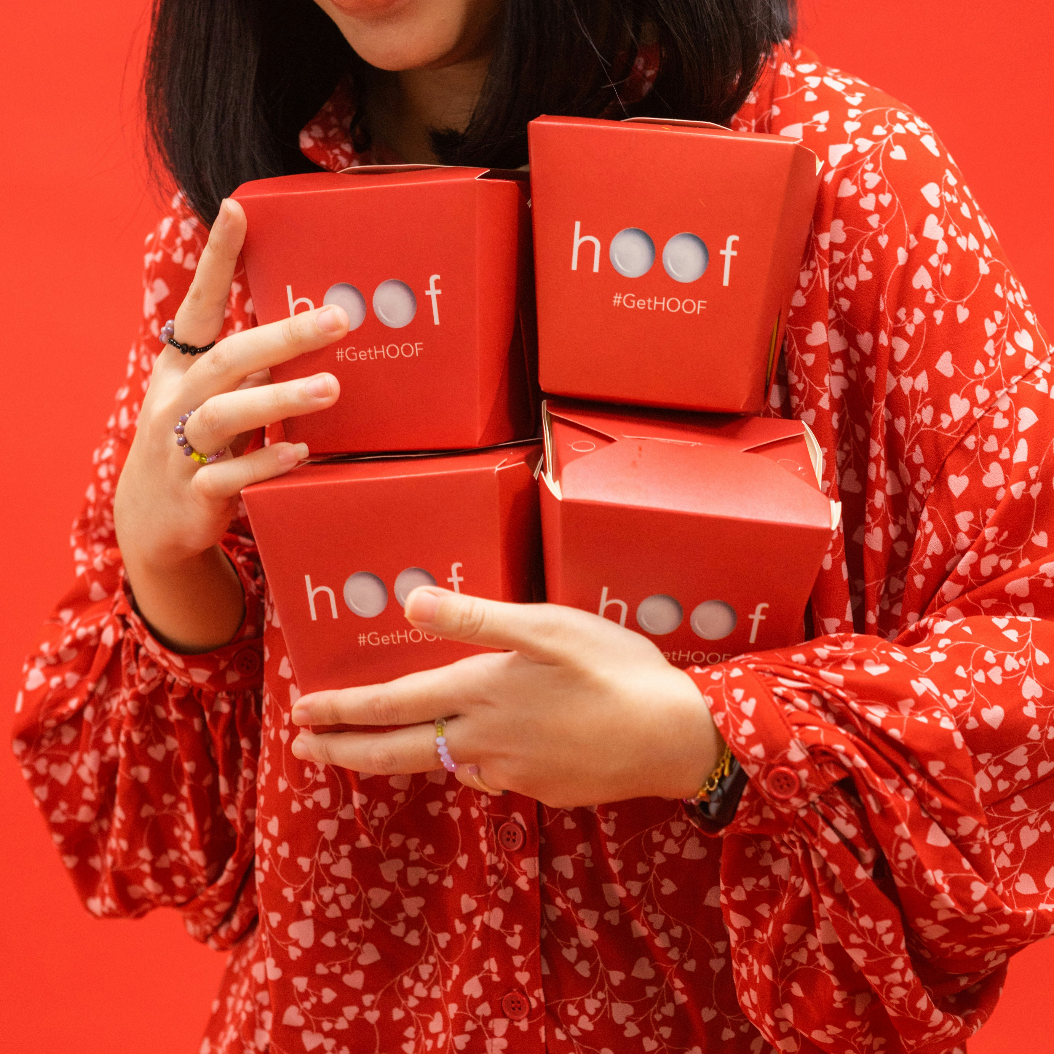 A person in a red heart-patterned shirt holding four red takeout boxes