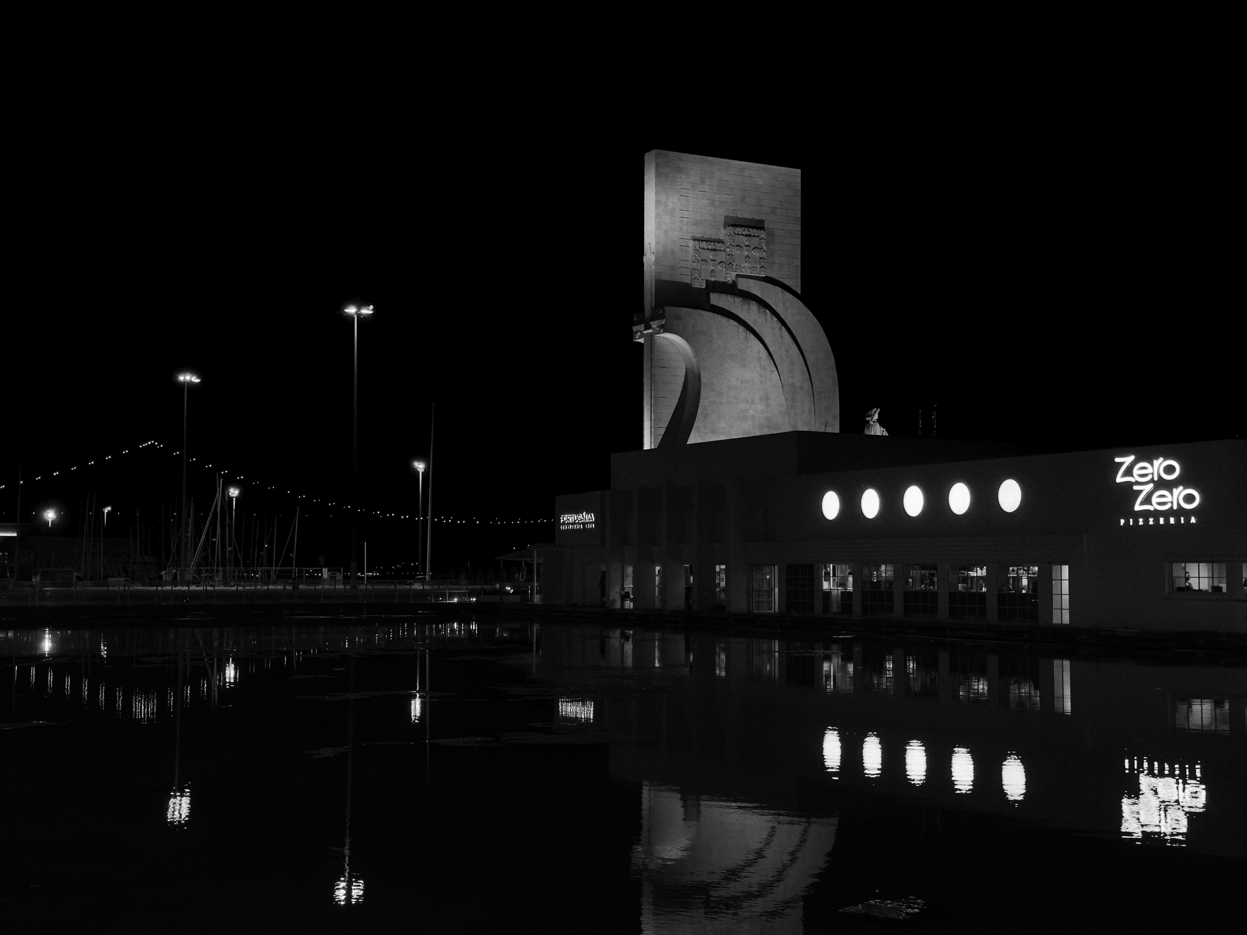 The Padrão dos Descobrimentos monument illuminated at night beside a waterfront building in Lisbon