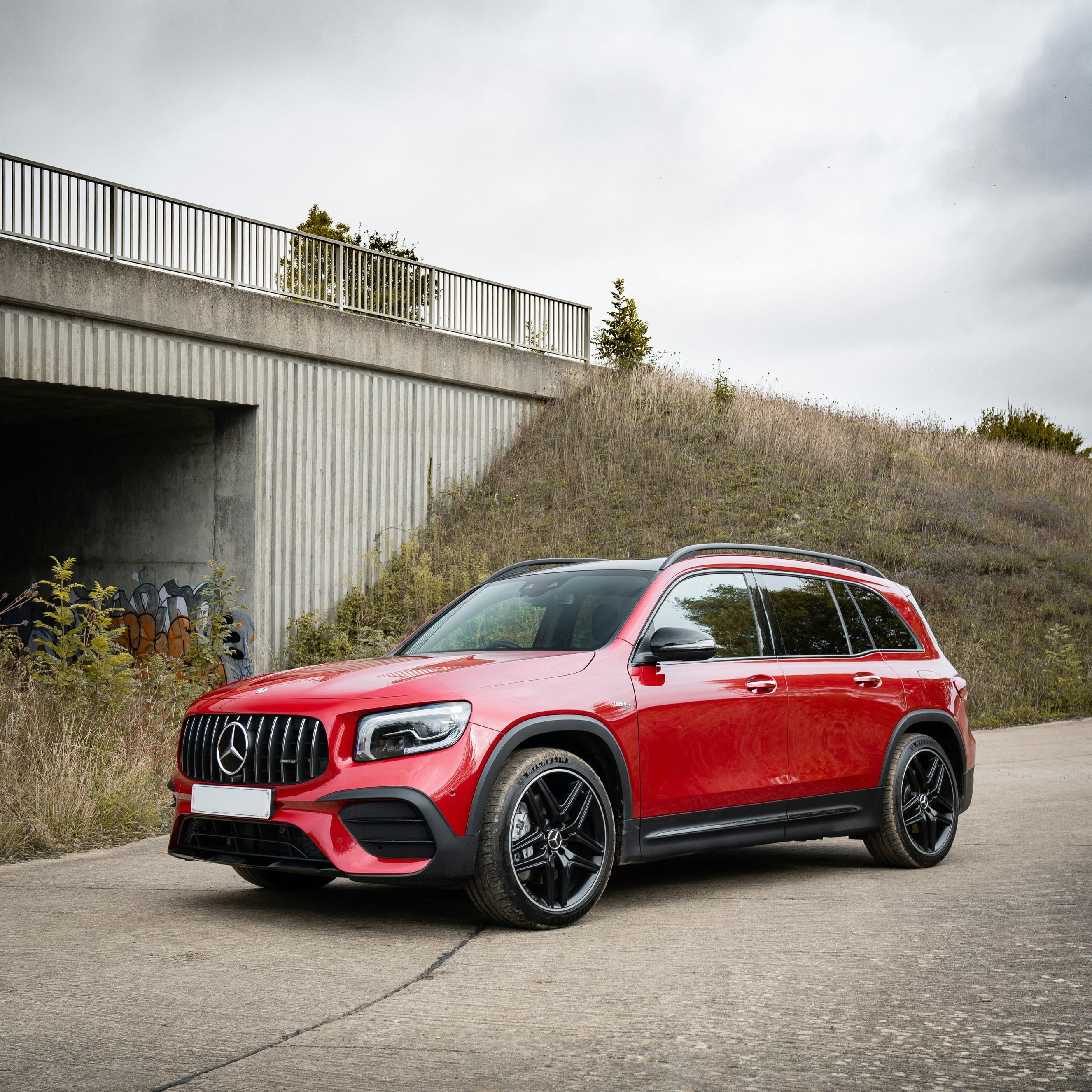 Um SUV vermelho estacionado em uma estrada de concreto sob uma ponte de concreto