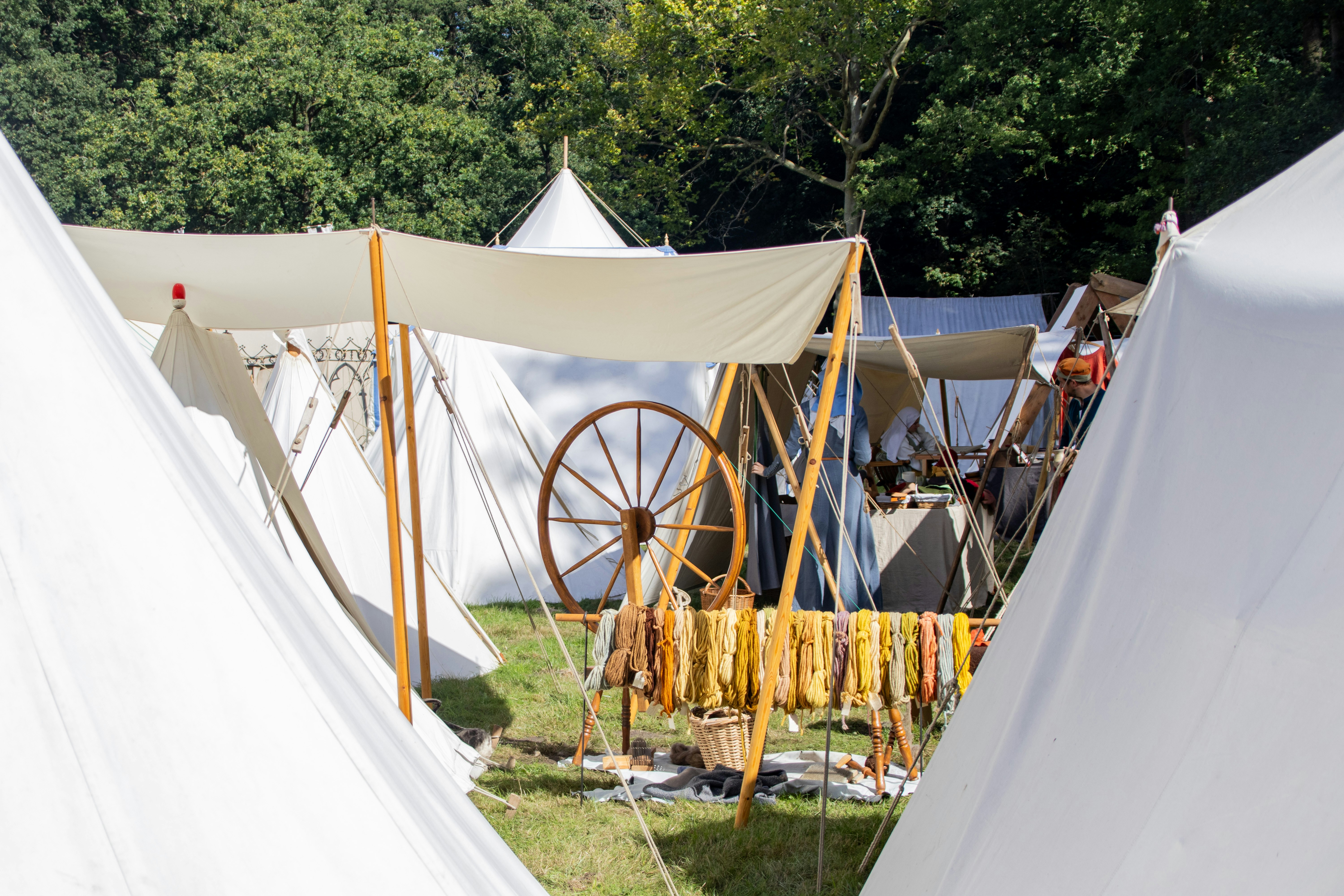 A spinning wheel and dyed yarn hanging between white canvas tents in a park