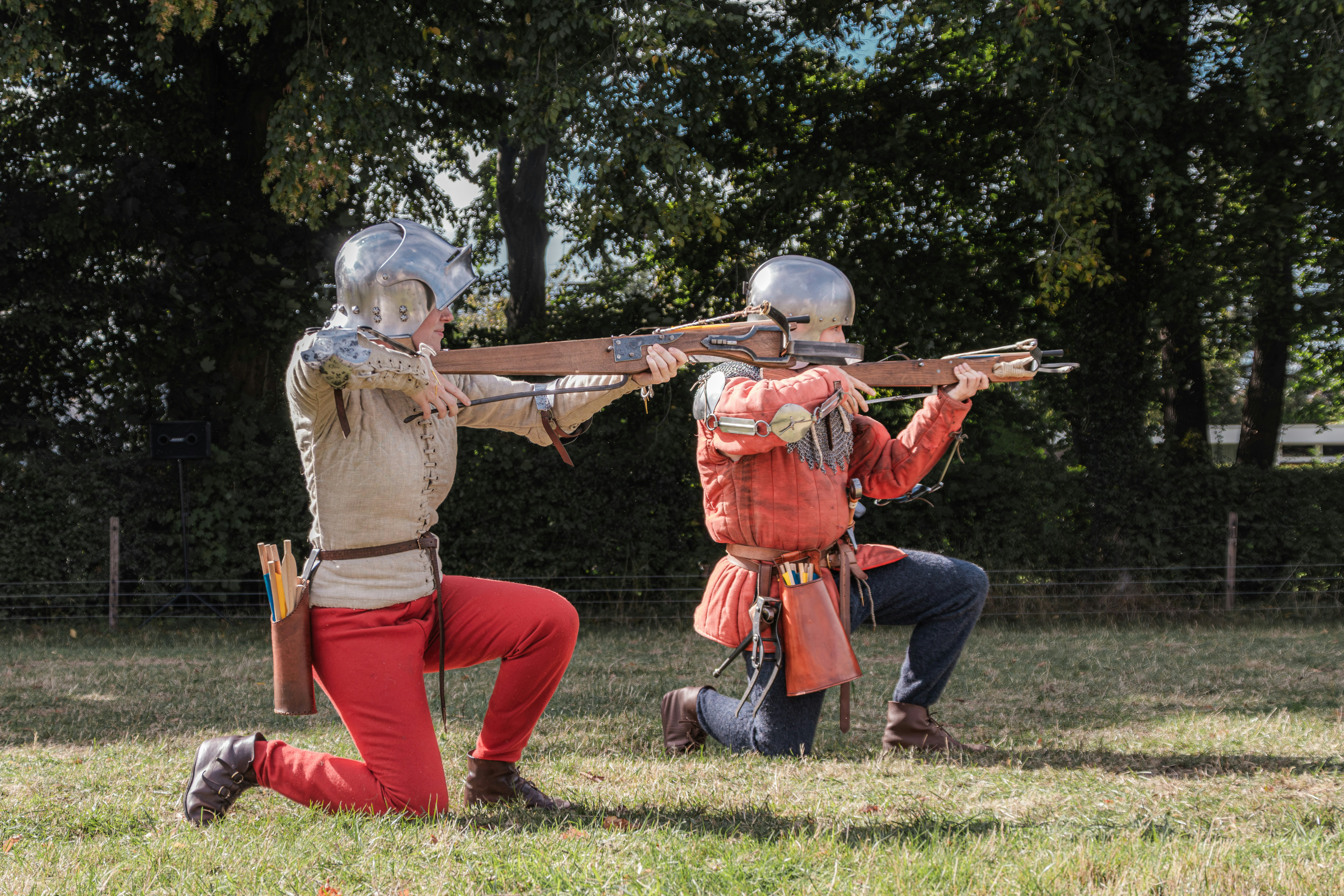 Two people in medieval armor kneeling and aiming crossbows in a grassy field