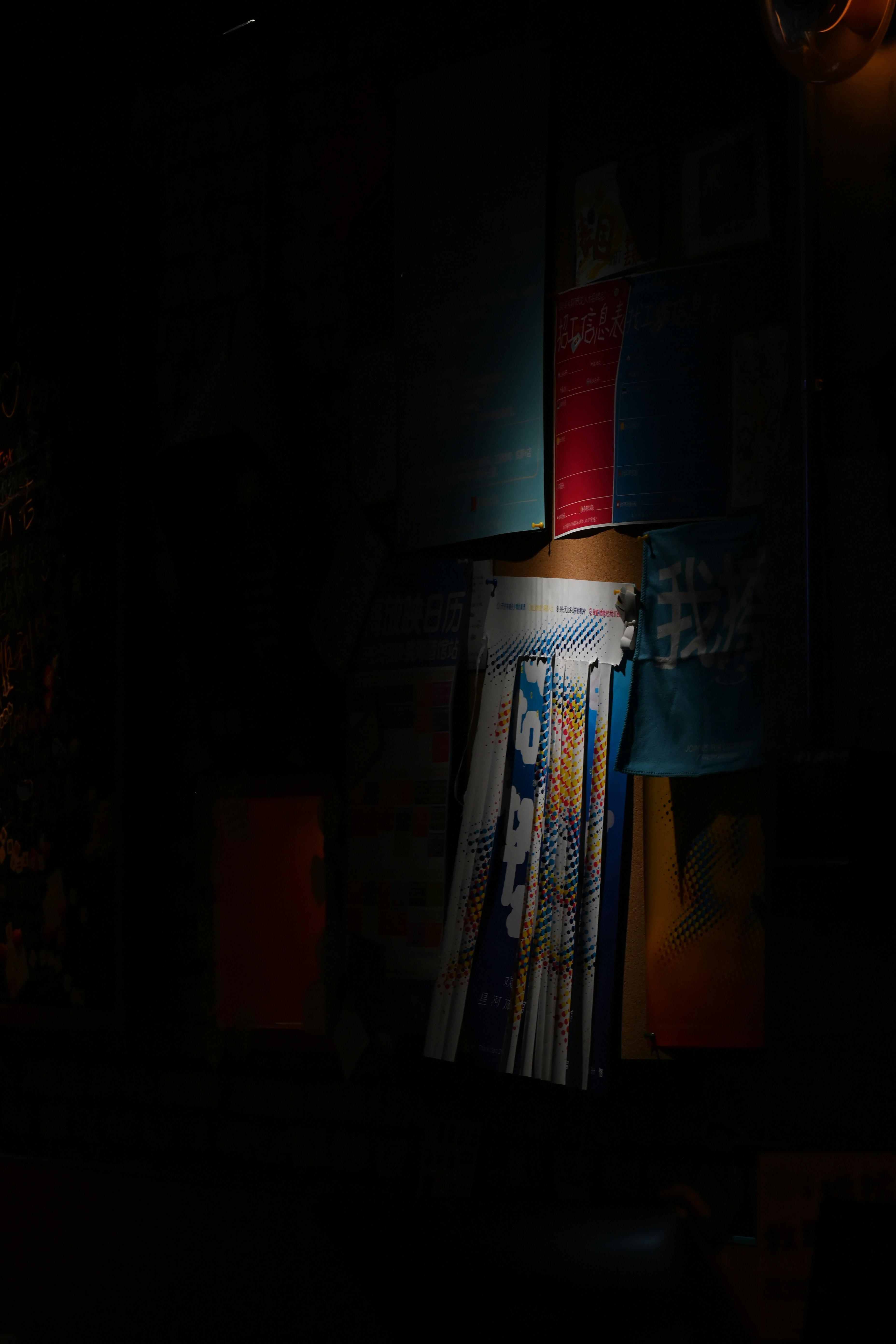 A cork bulletin board with colorful posters and notices in dim lighting