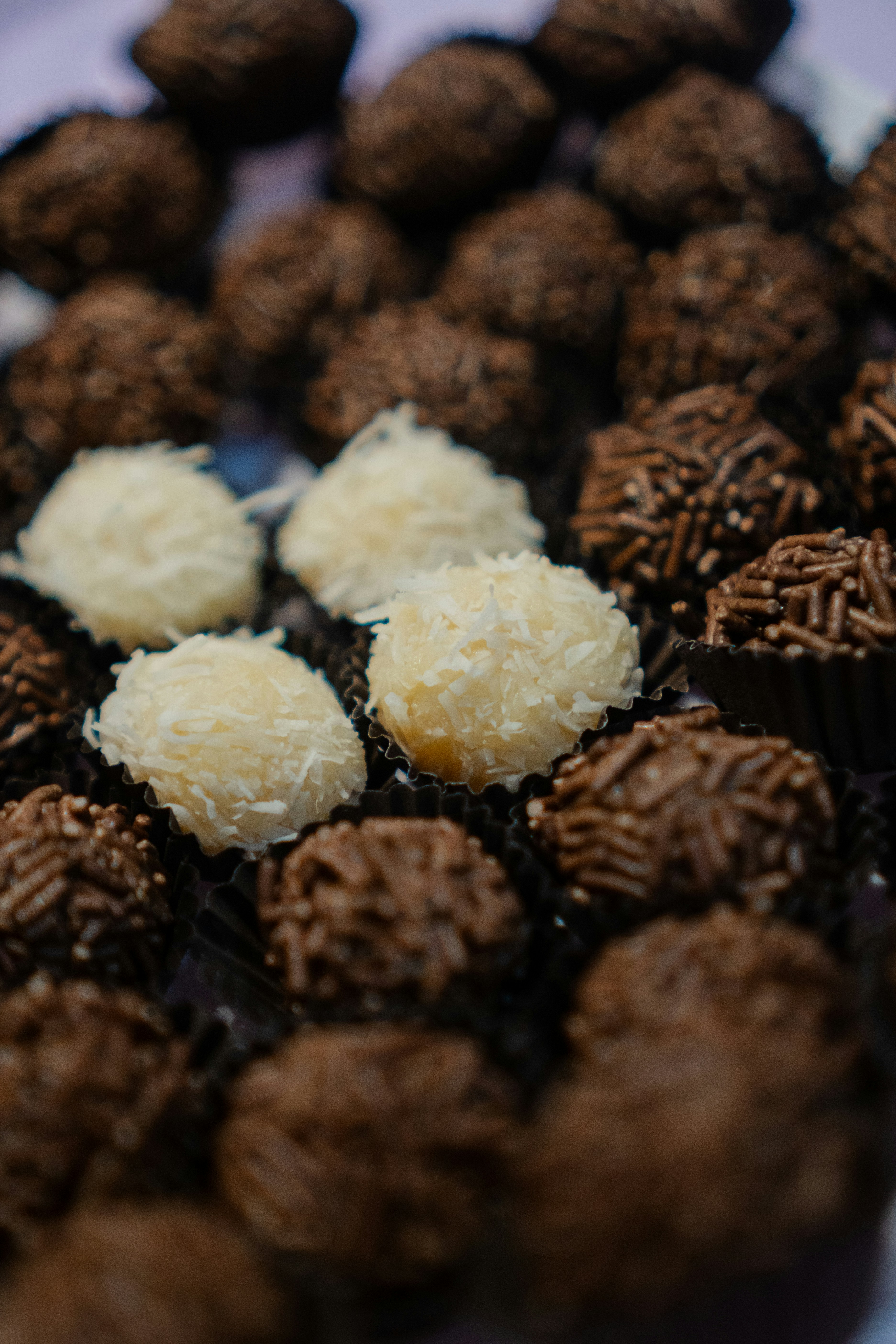 A group of chocolate brigadeiros and coconut beijinhos in small paper cups