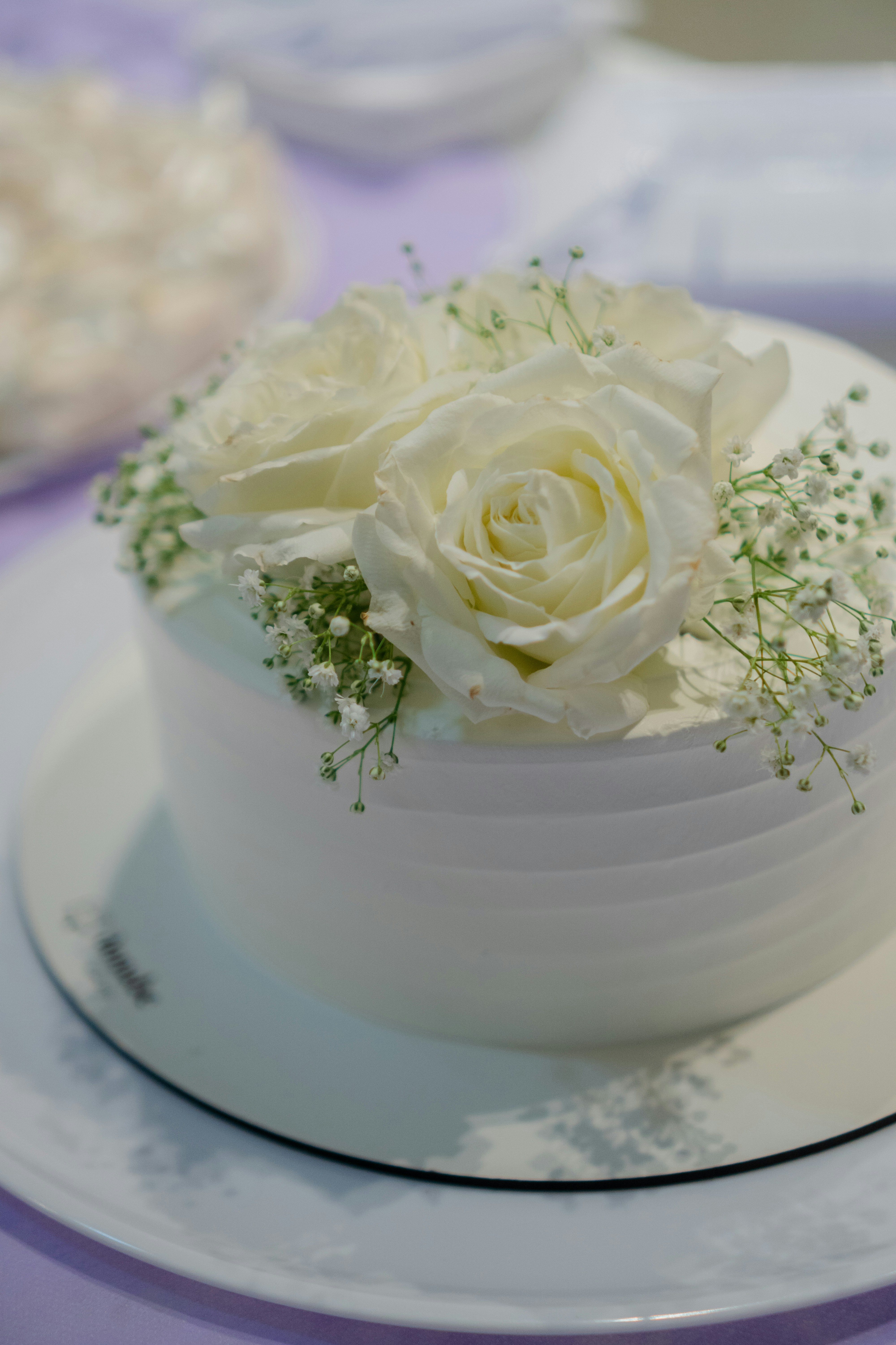 A white cake topped with white roses and baby's breath on a plate
