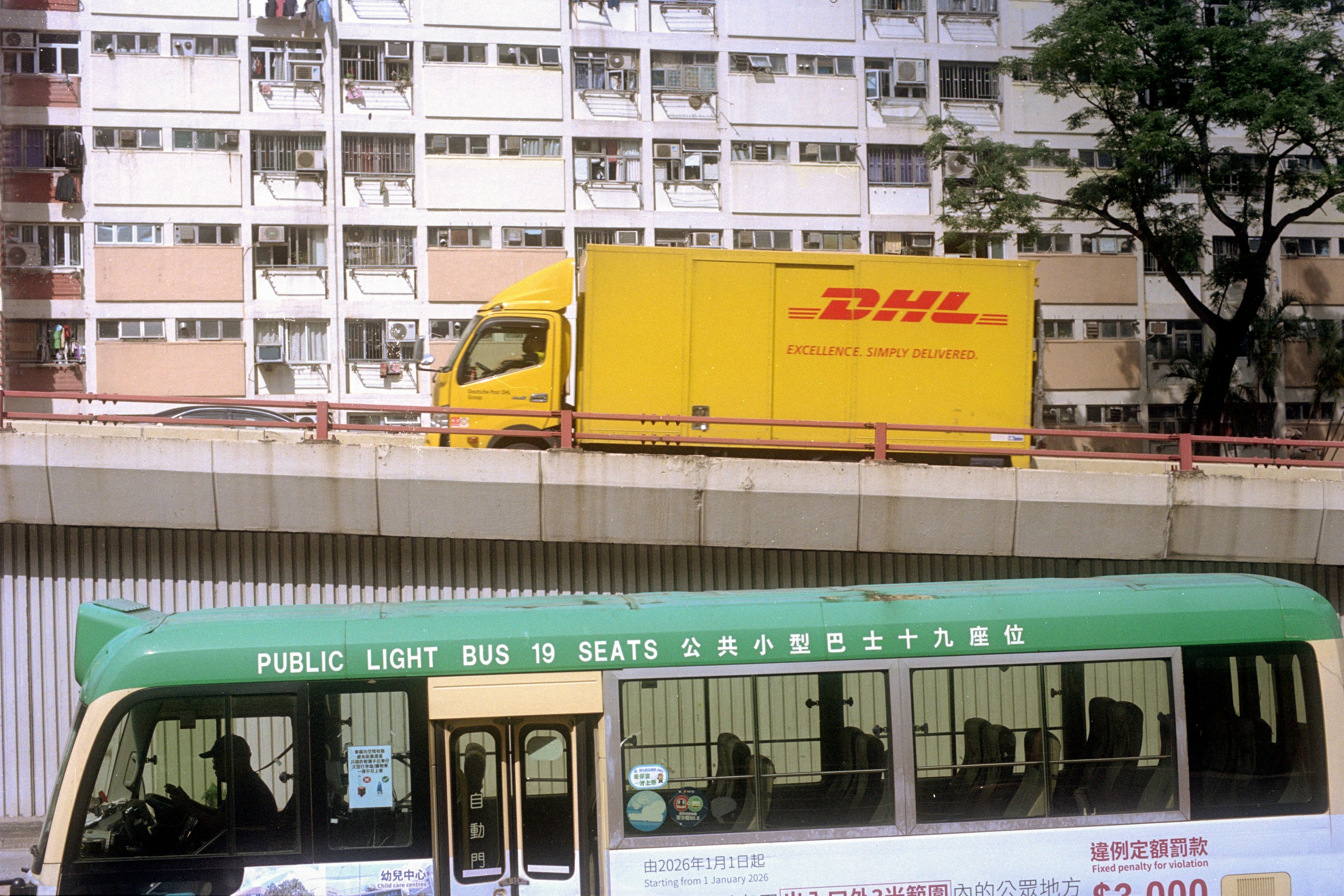 Un camion DHL giallo su un cavalcavia sopra un autobus verde a luce pubblica