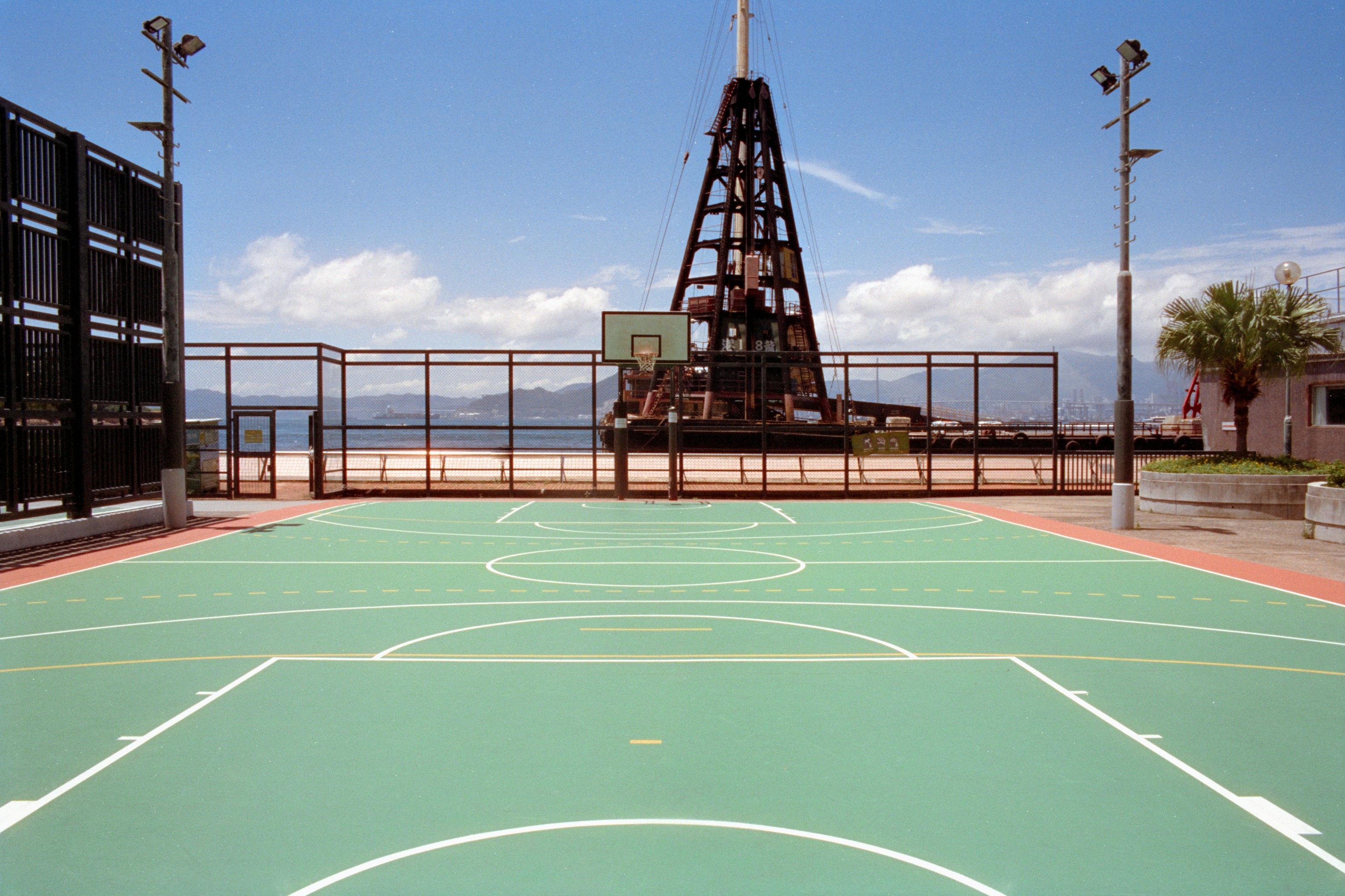 An outdoor green basketball court by the sea with a large industrial crane