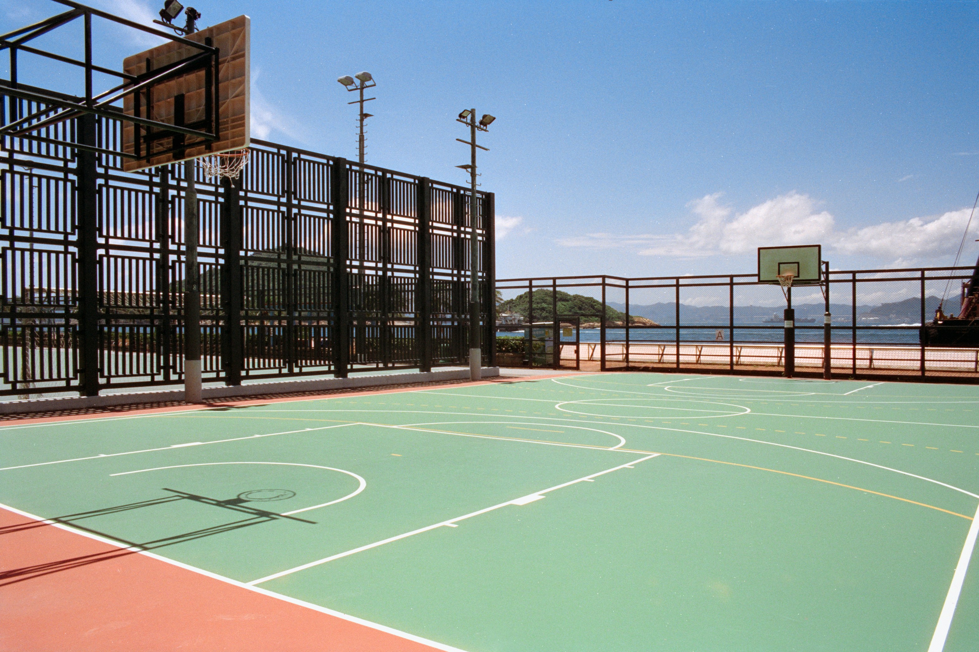 An outdoor basketball court with green flooring beside a metal fence and ocean