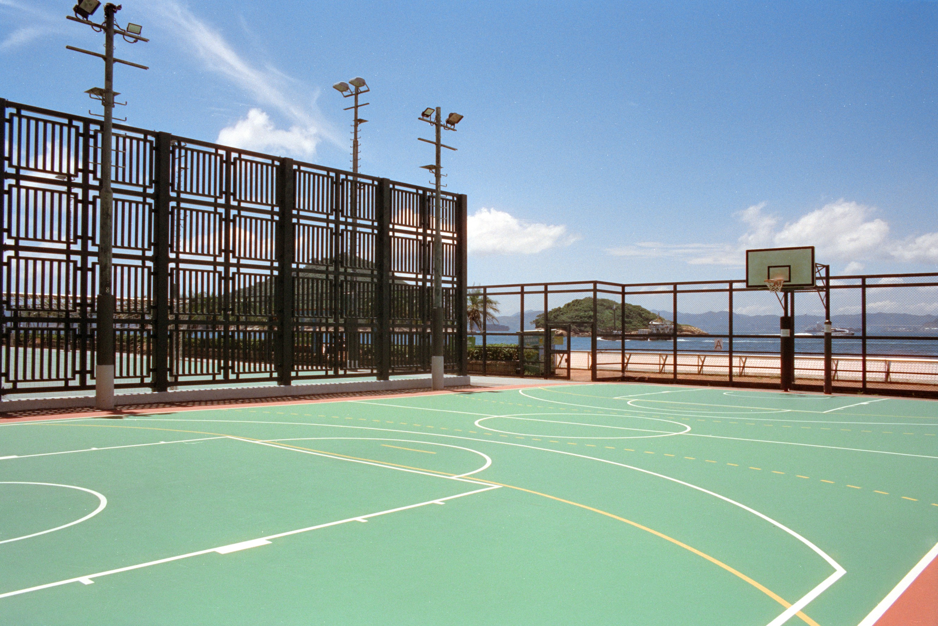 A green basketball court with white lines beside a beach and ocean
