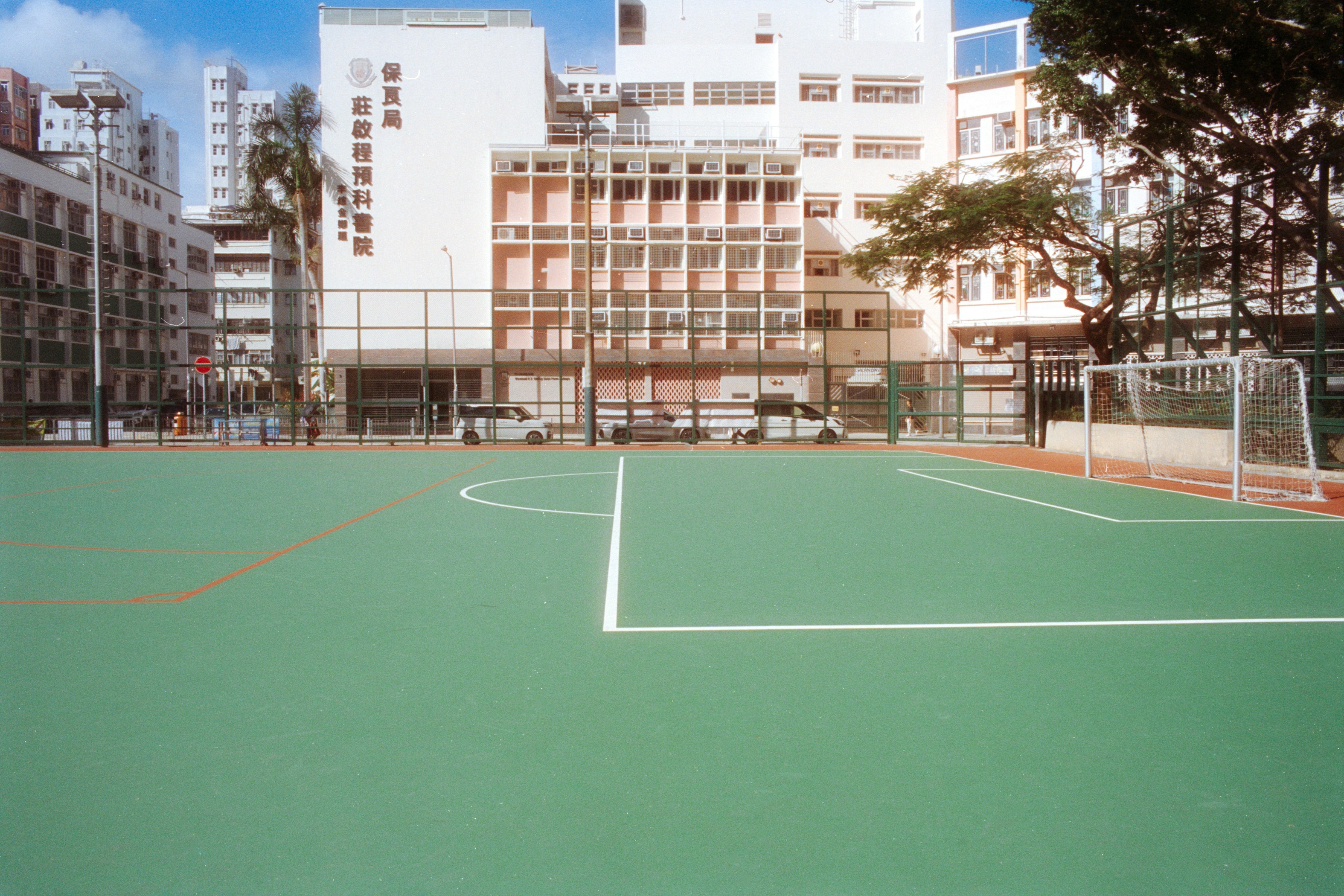 A green soccer court with white lines and a goal in an urban area