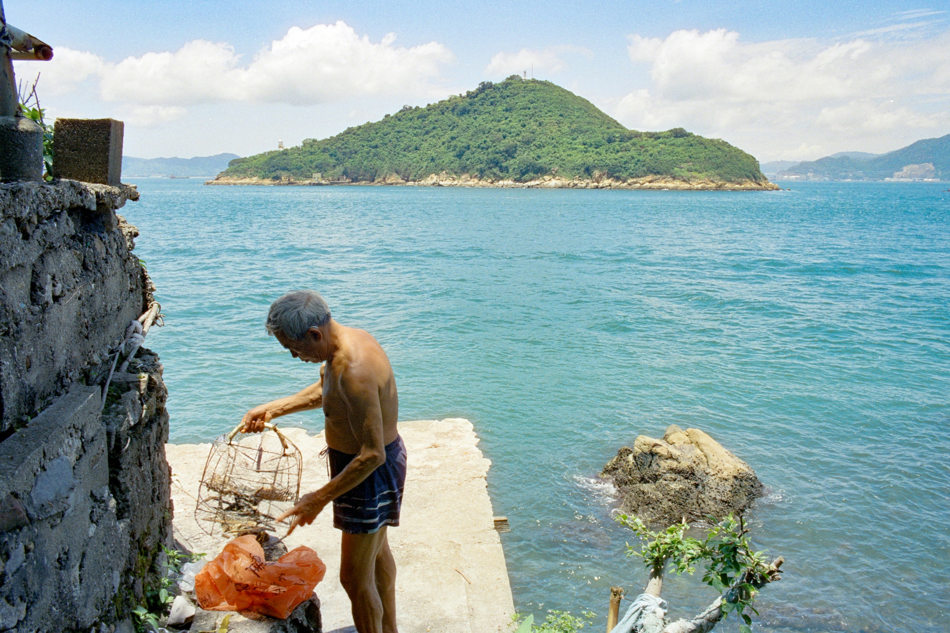 An older man holding a wire fishing trap on a concrete pier by the sea